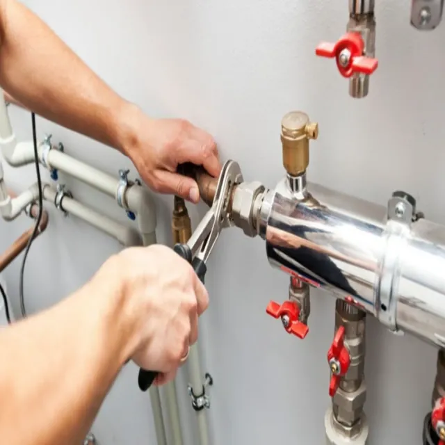 Plumber using a wrench on a pipe. White pipes with red valves on a white wall.