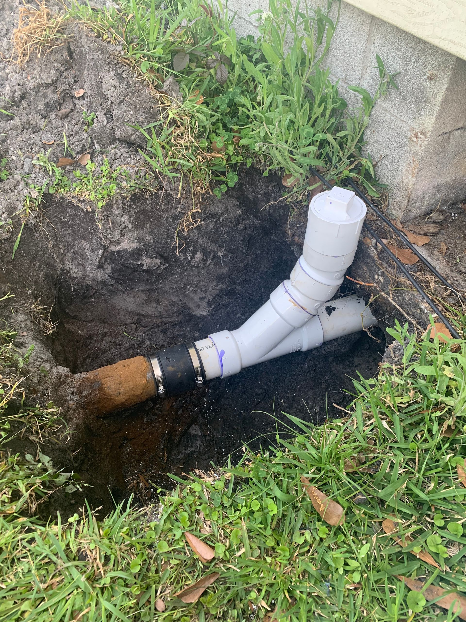 PVC pipes emerging from dirt, joined and extending from the ground, in a grassy setting.