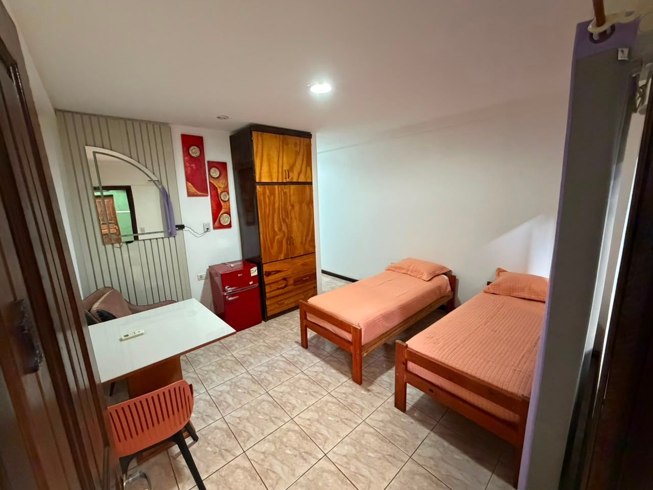 Small bedroom with two single beds, wardrobe, desk, mirror, and tiled floor