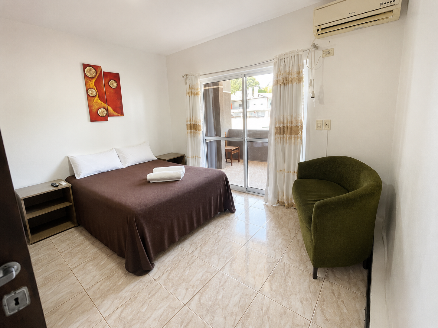 Small bedroom with a bed, green chair, balcony doors, and air conditioner.