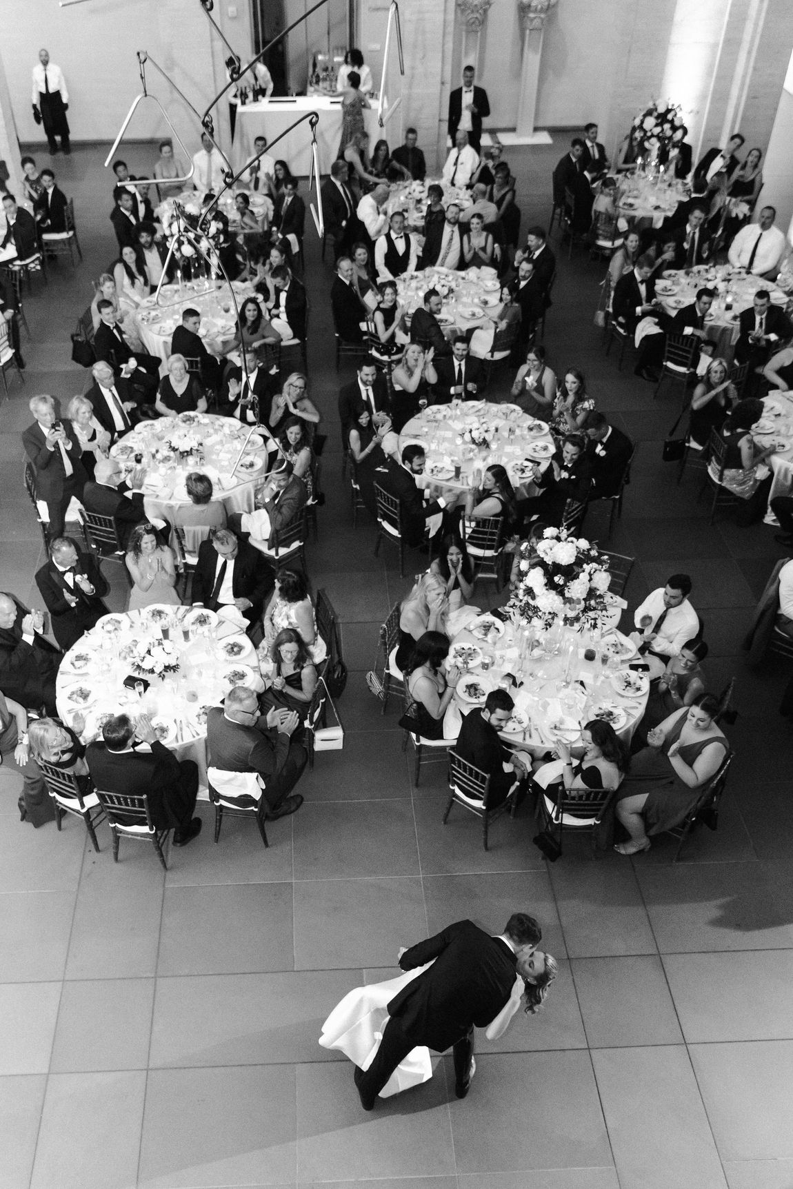 A bride and groom are dancing in front of a crowd of people at a luxury museum wedding reception.