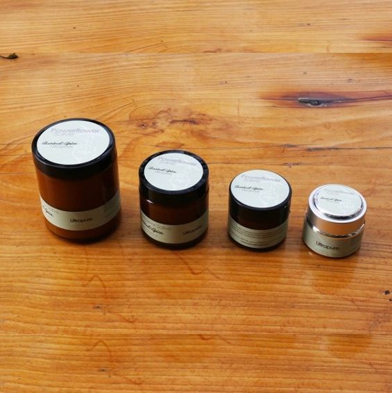 Four small dark jars with white lids lined up on a wooden table.