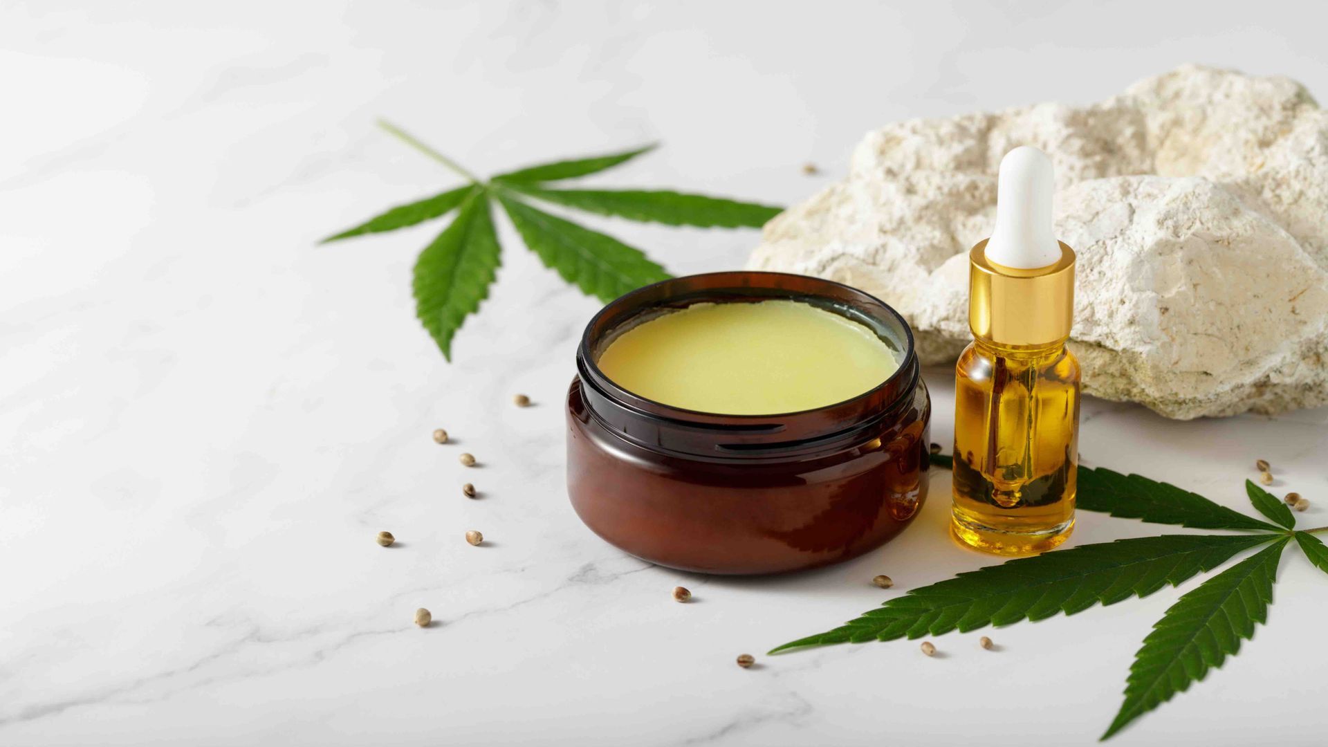 Cannabis skincare cream jar and dropper bottle with hemp leaves and powder on a white background