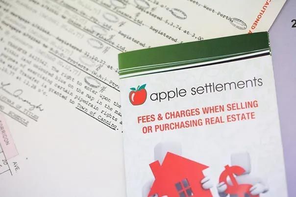 Apple Settlements brochure on fees and charges for purchasing real estate, with papers in the background Apple Settlements brochure on fees and charges for purchasing real estate, with papers in the background