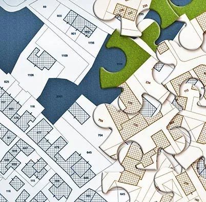 Close-up of interlocking jigsaw puzzle pieces with blue, green, and tan sections over a floor plan. Close-up of interlocking jigsaw puzzle pieces with blue, green, and tan sections over a floor plan.