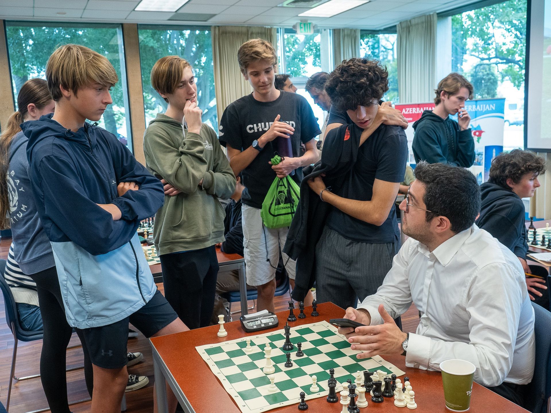 A group of people are standing around a table with a chess board.