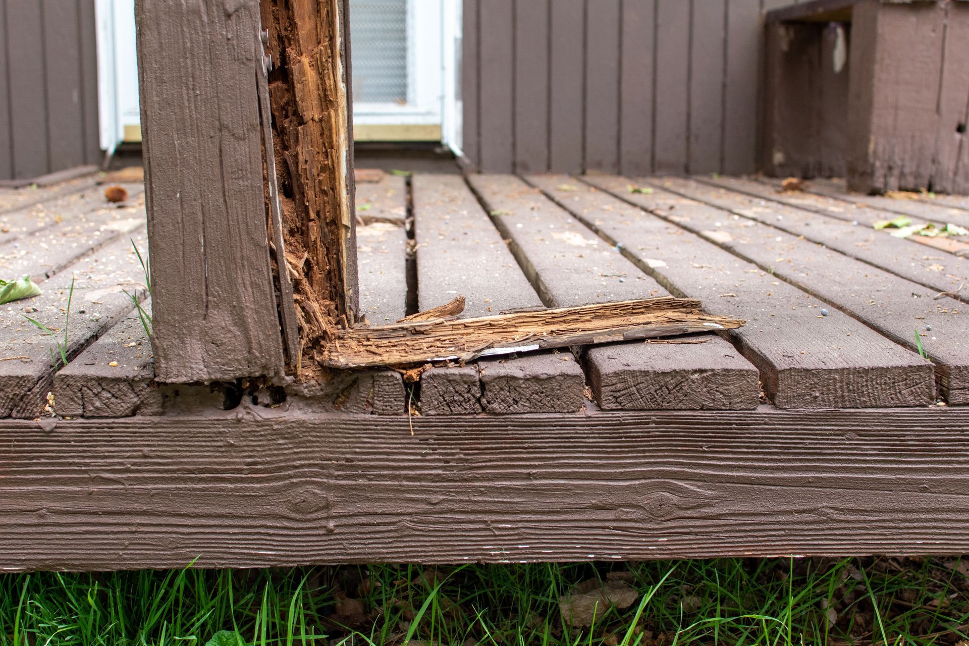 Weathered wooden deck with a damaged railing post and broken boards near the edge