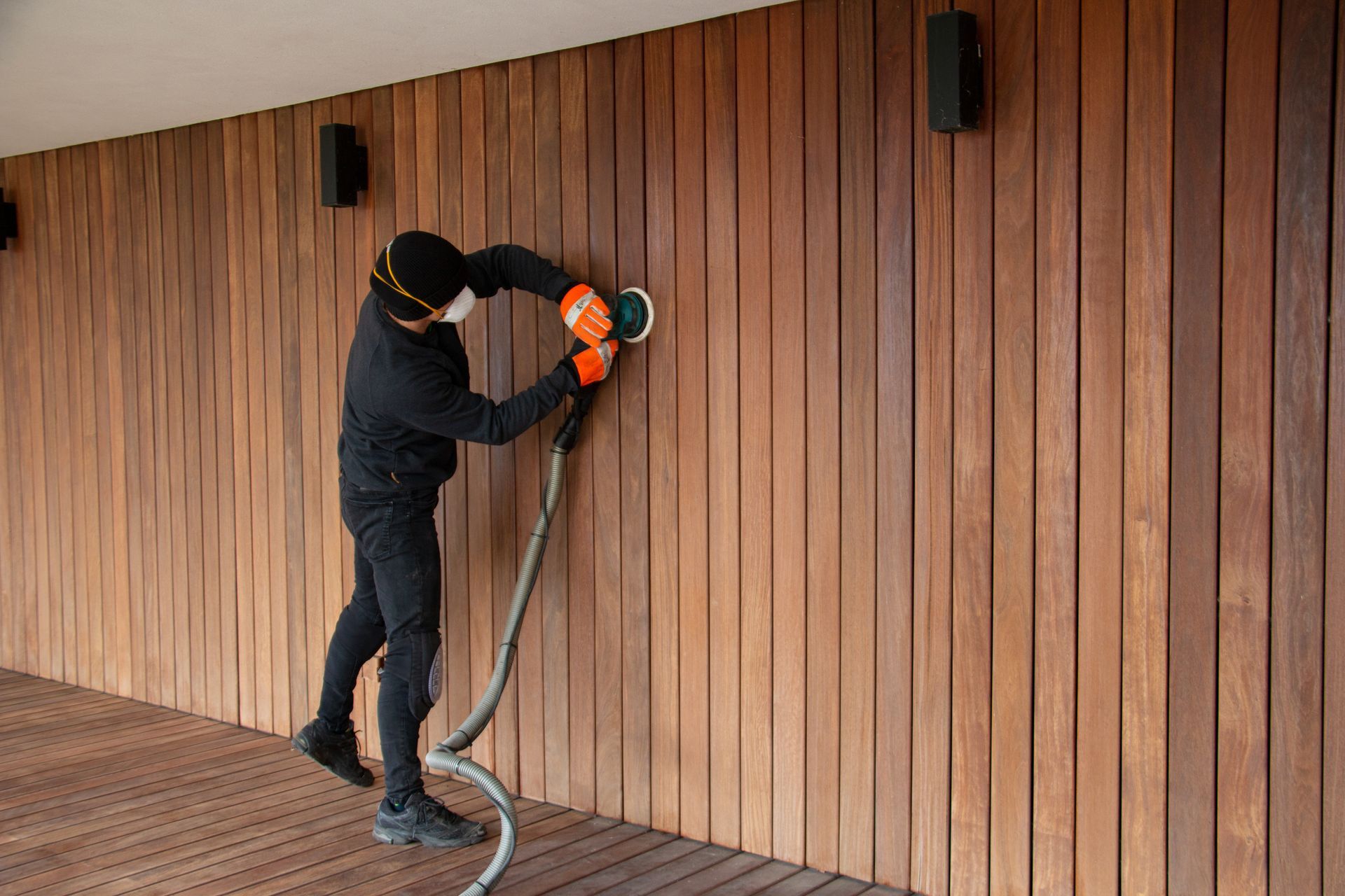 Worker sanding a wooden wall with a power tool on an outdoor deck