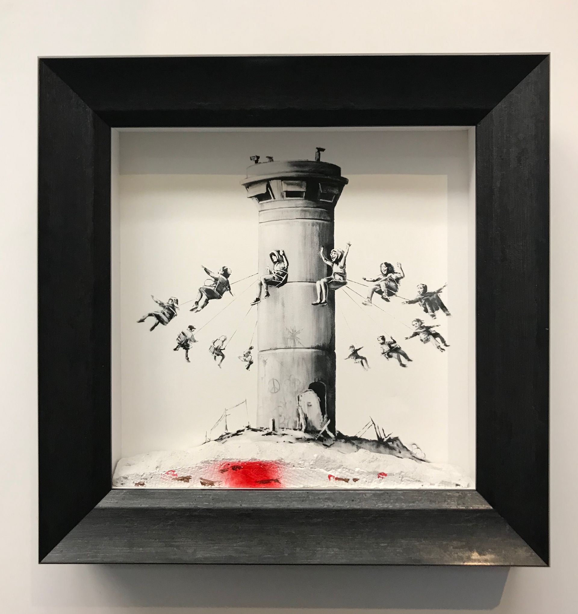 A framed art piece shows people on swings attached to a watchtower, with a red stain on the ground below.