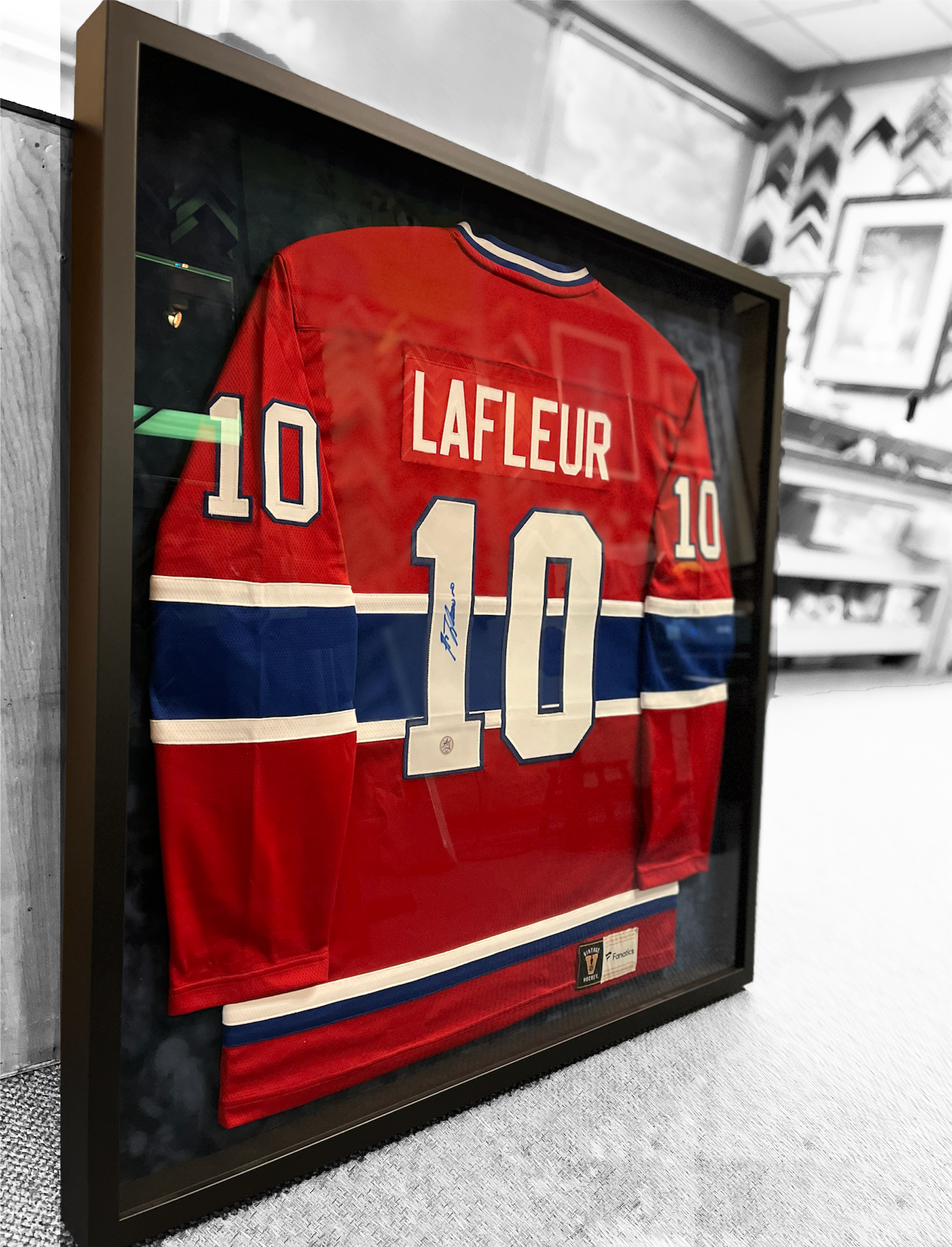 A framed, autographed Montreal Canadiens Guy Lafleur jersey in red, blue, and white, displayed in a framing shop.