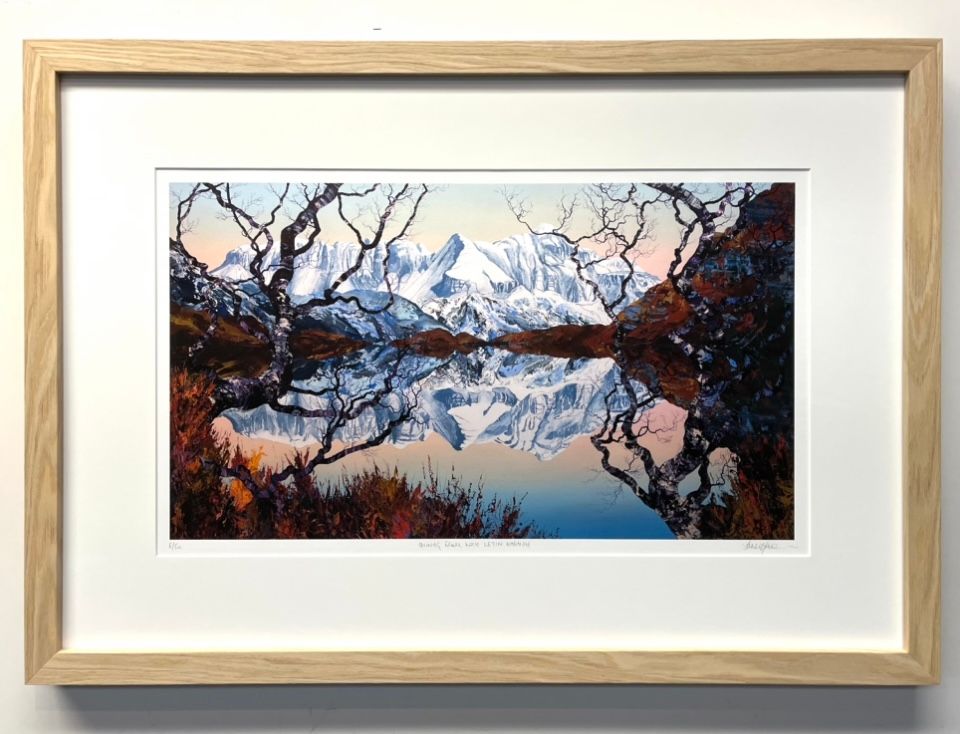 A framed landscape painting of snow-capped mountains reflecting in a still lake, framed by bare, silhouetted tree branches.