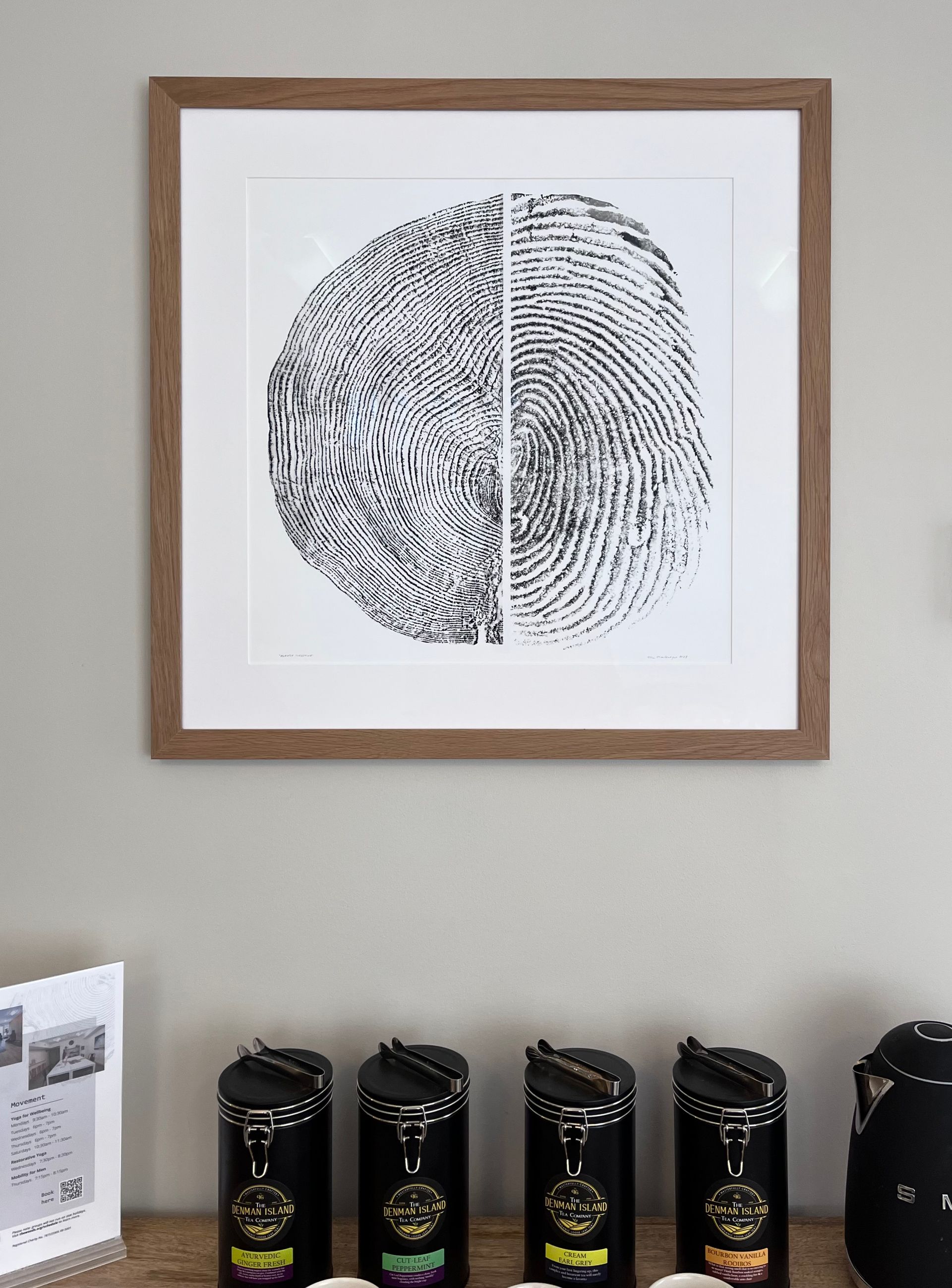 Framed art of a split fingerprint hanging above a row of four black canisters on a shelf.