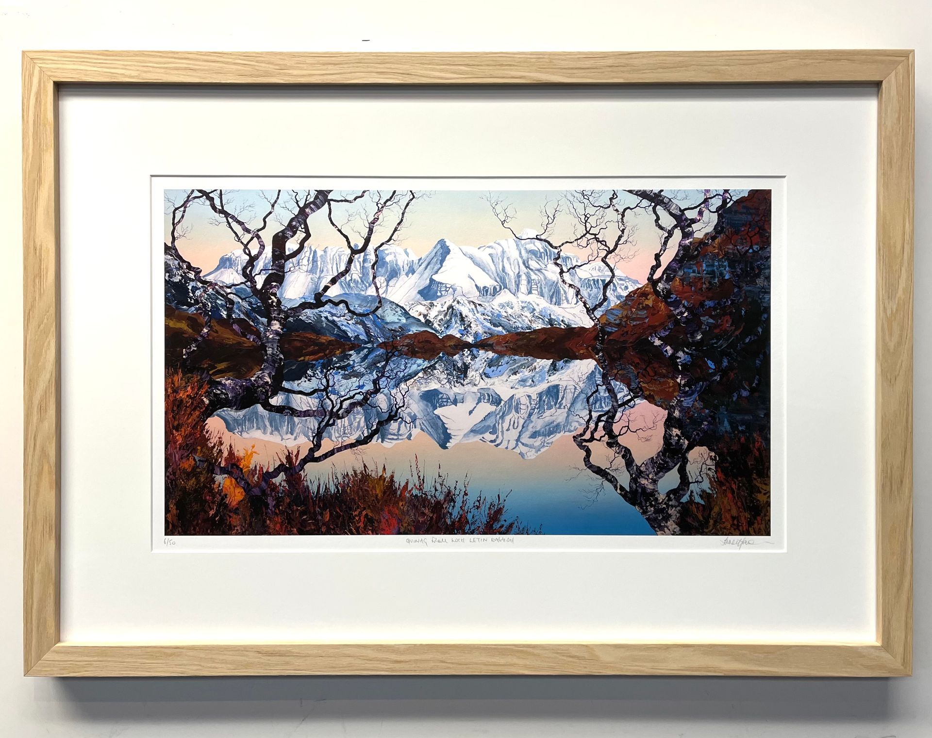 Framed print of snow-capped mountains reflecting in a still lake, framed by dark tree silhouettes in autumn tones.