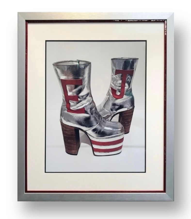 Framed artwork of a pair of silver platform boots with red striped soles and the letters 