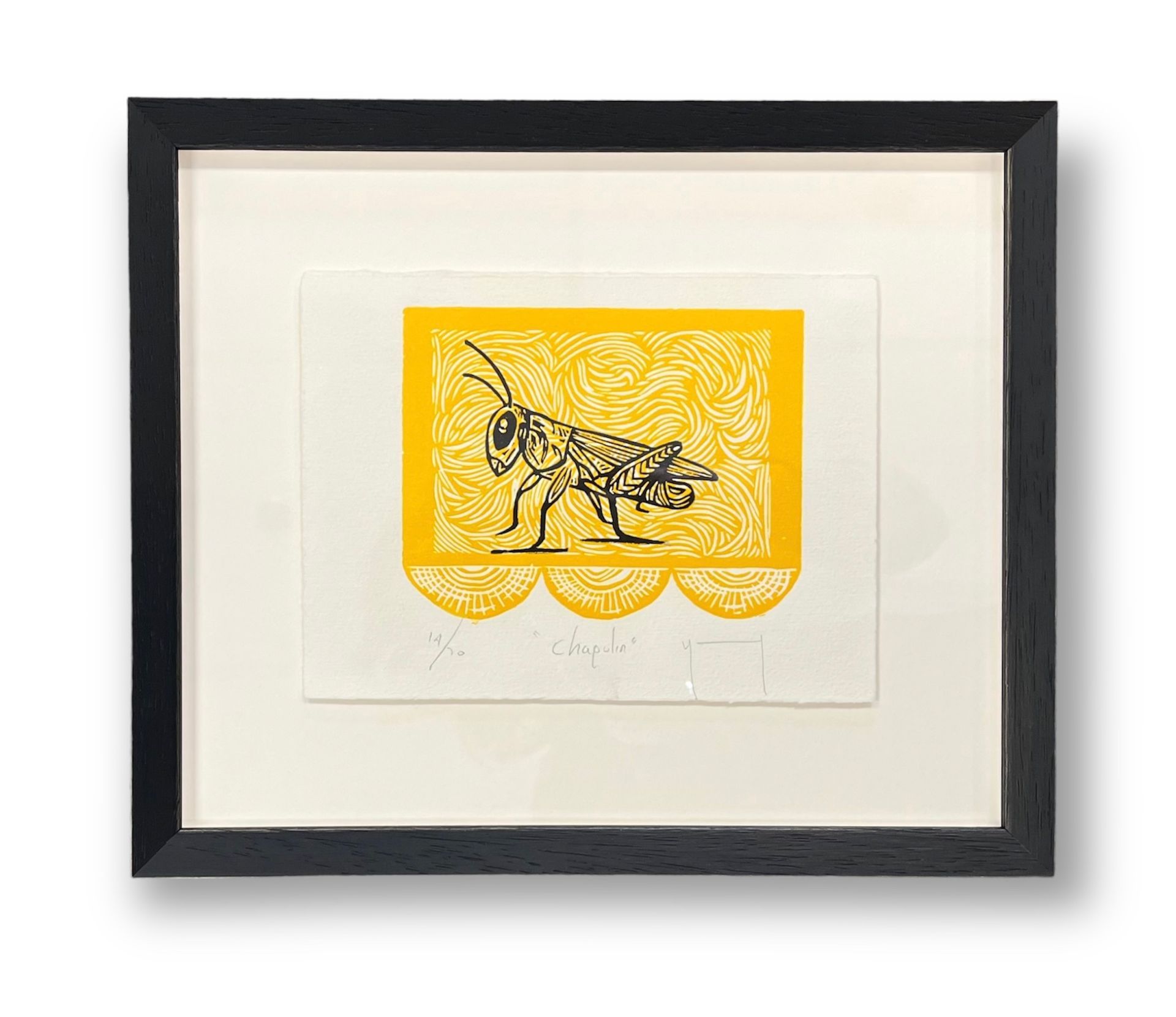 A framed, rectangular linocut print featuring a detailed black grasshopper against a bright yellow background.