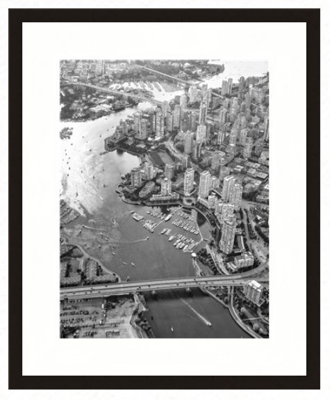 Aerial black-and-white view of a city waterfront, featuring high-rise buildings, a marina, and a bridge crossing a river.