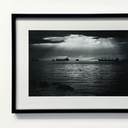 A framed black-and-white photograph shows silhouettes of cargo ships on the water under dramatic rays of light.