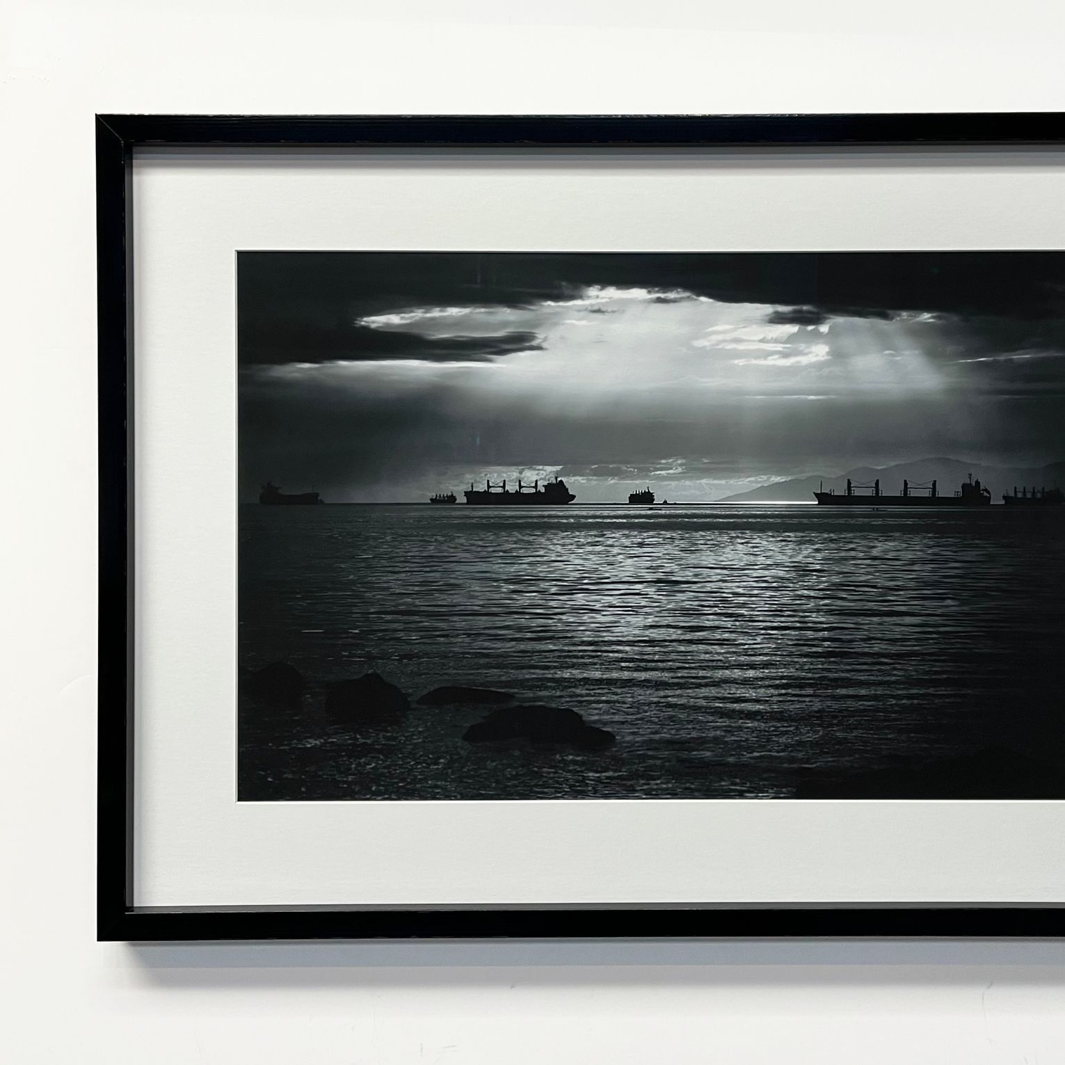 A framed black-and-white photograph shows silhouettes of cargo ships on the water under dramatic rays of light.