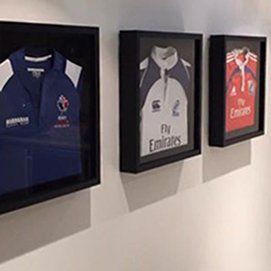 Three sports jerseys displayed in black shadow box frames mounted on a plain white wall.