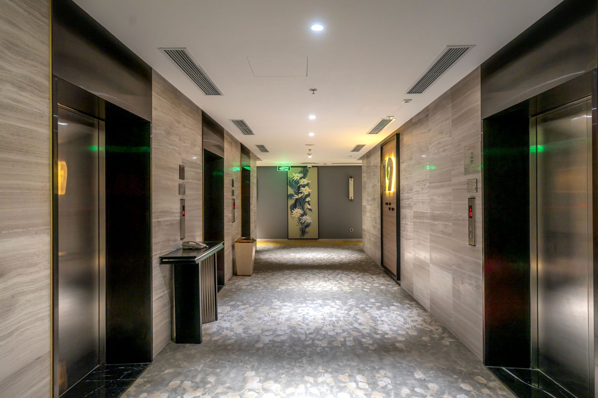 Modern hotel hallway with elevators, gray carpet, and soft ceiling lights