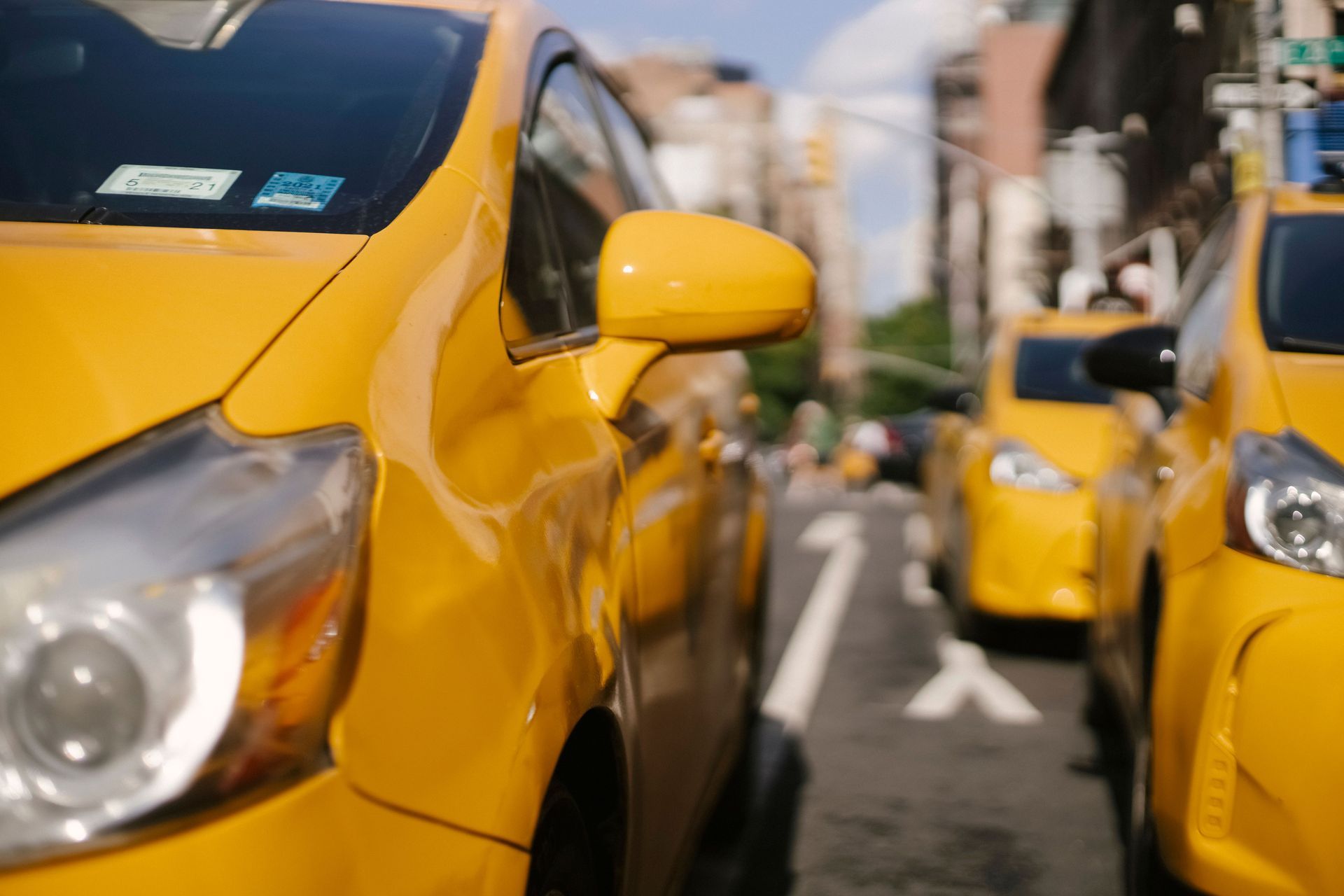 Yellow taxis lined up on a city street, with a close-up of one taxi in the foreground