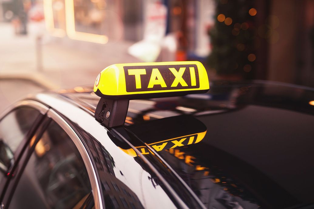 Yellow TAXI sign on top of a black car in a city street scene.