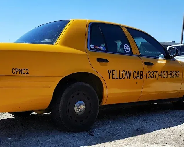Yellow taxi cab parked outdoors, side view with black lettering and phone number on the door.