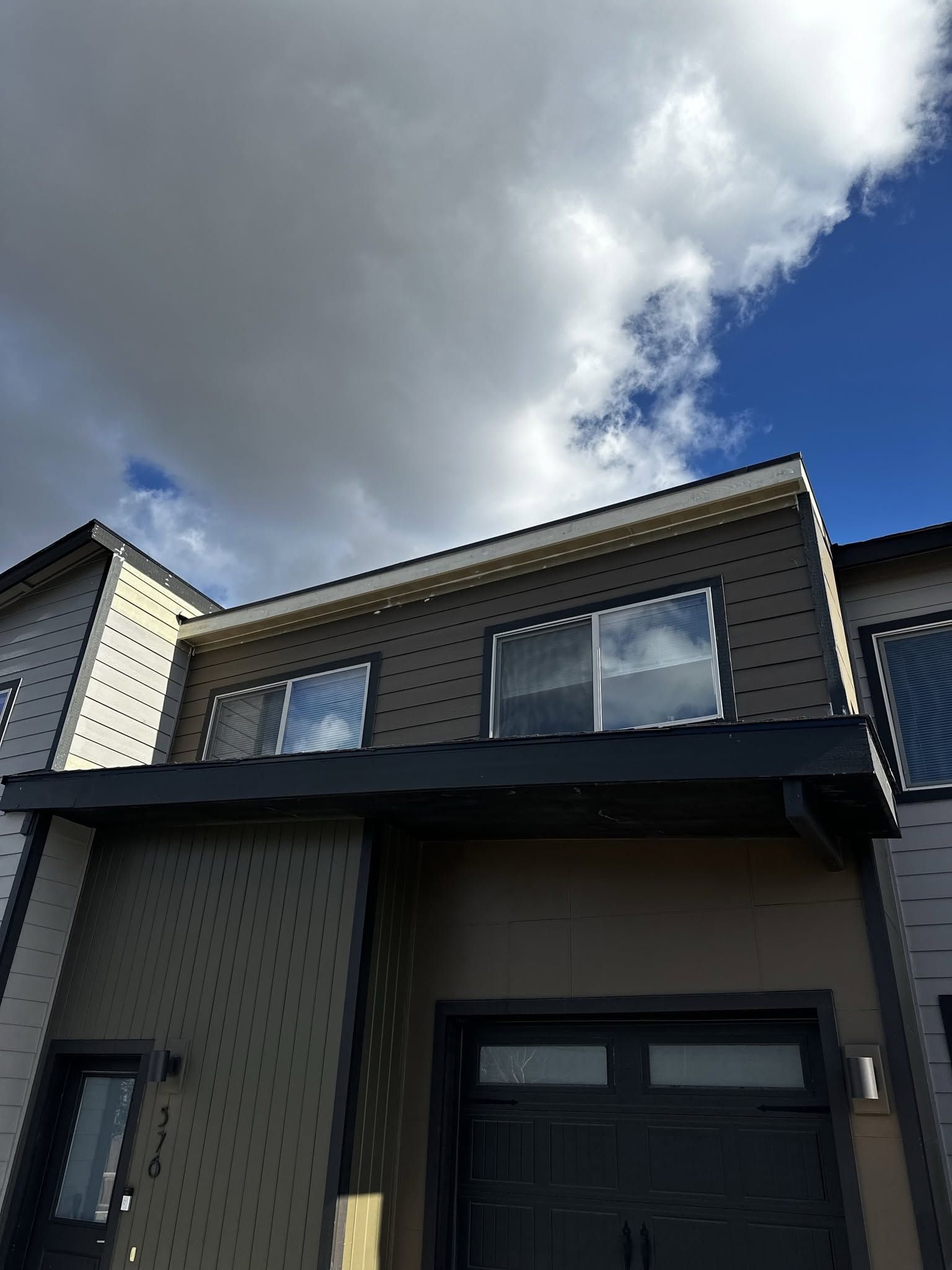 Modern two-story house with gray siding, dark trim, and a partly cloudy sky above