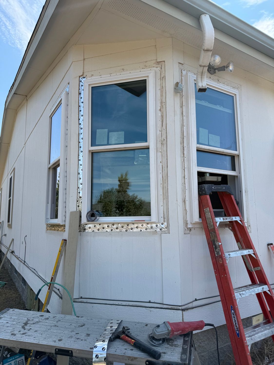 White house exterior with windows, ladder, and tools on the ground during repairs
