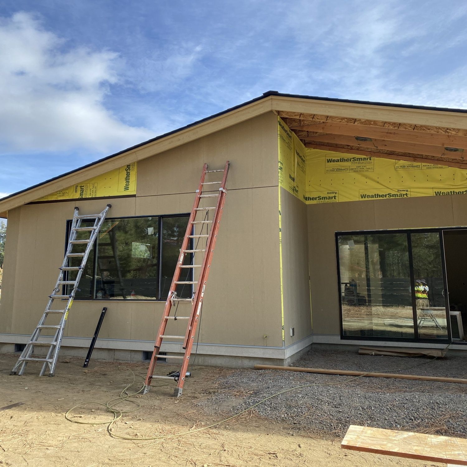 New building under construction with ladders, windows, and yellow sheathing under a blue sky