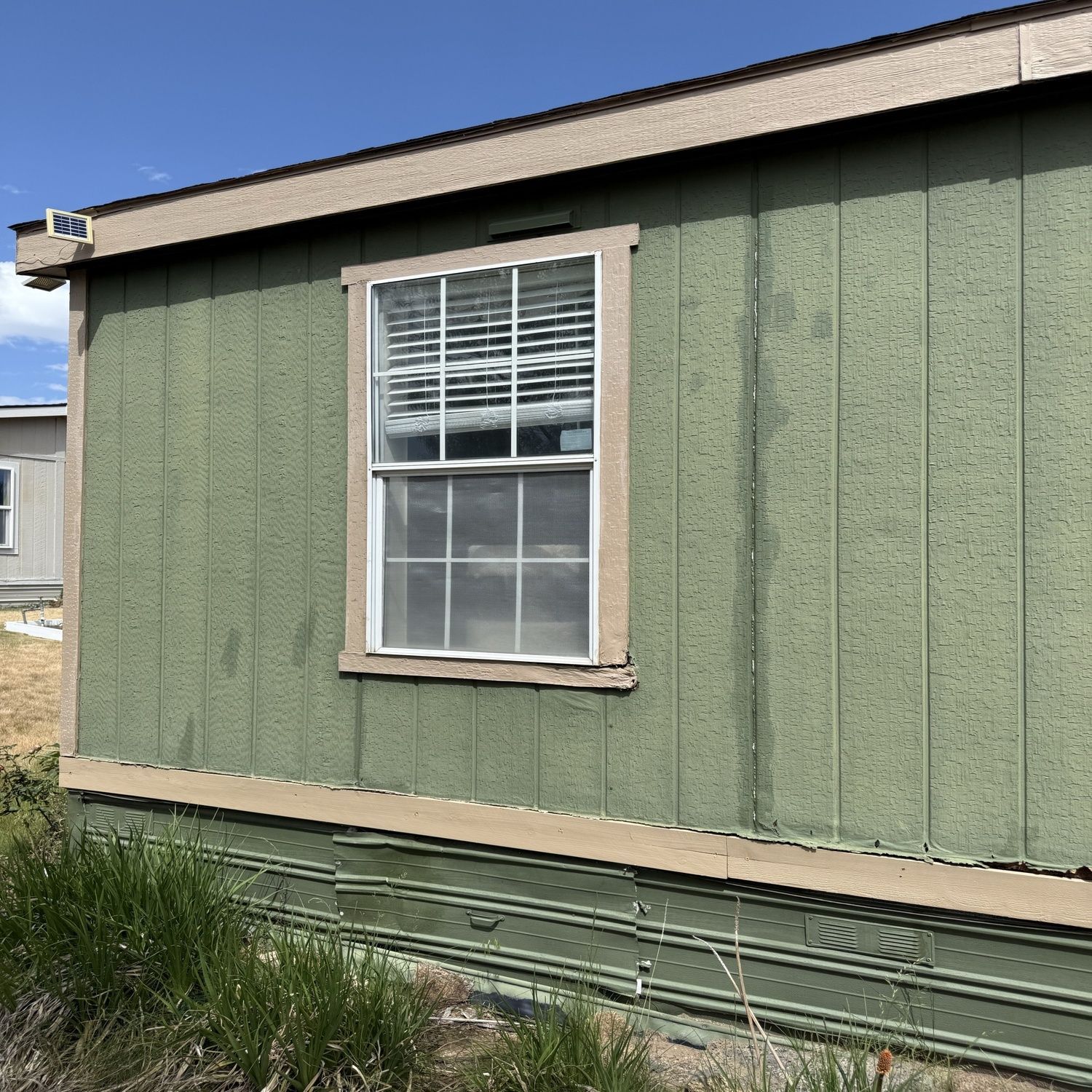 Green mobile home wall with a white window and small patch of grass in front