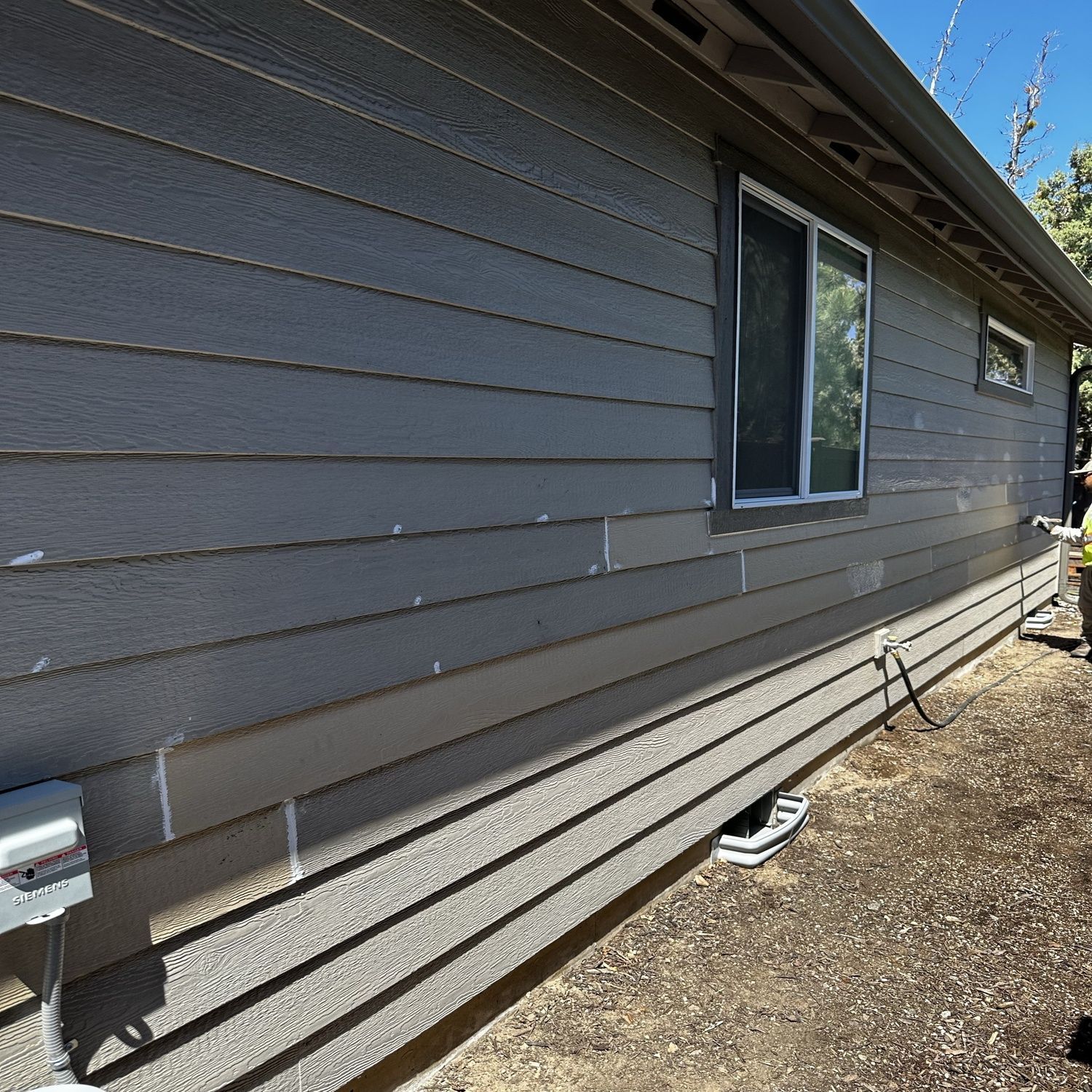 Side view of a gray house with horizontal siding, a window, and a gravel yard.
