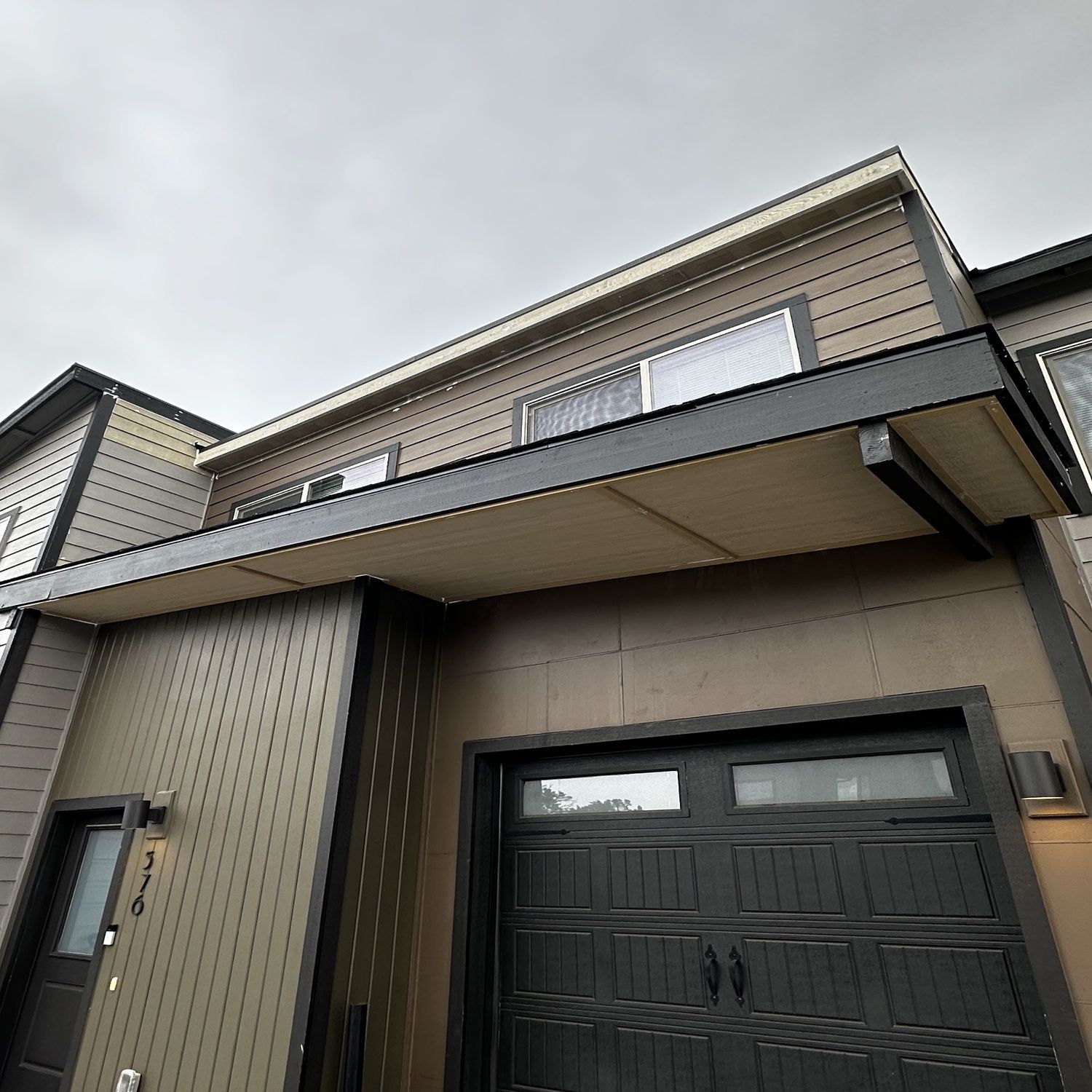 Modern townhouse exterior with beige siding, a black garage door, and a covered driveway.