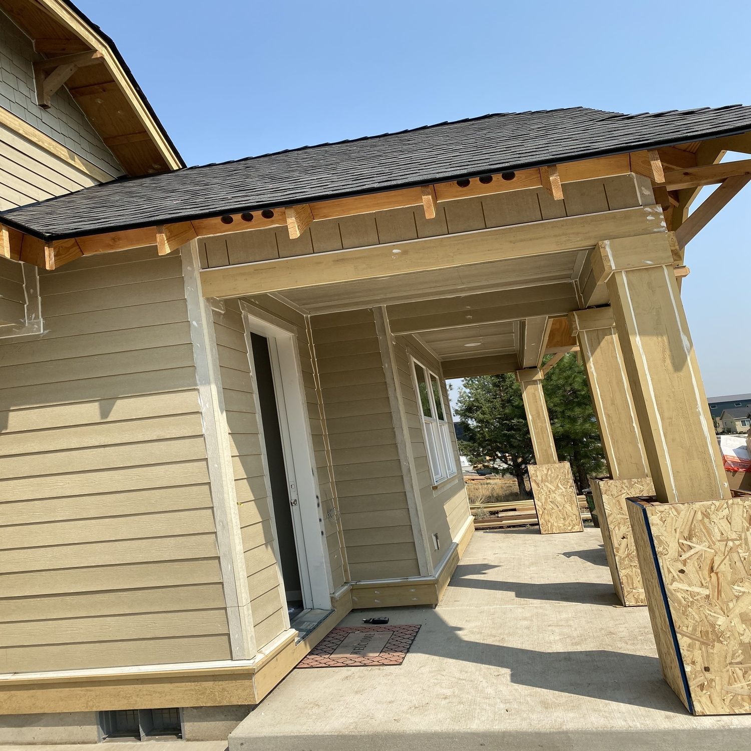 Tan house exterior with a covered front porch and tiled roof in bright sunlight