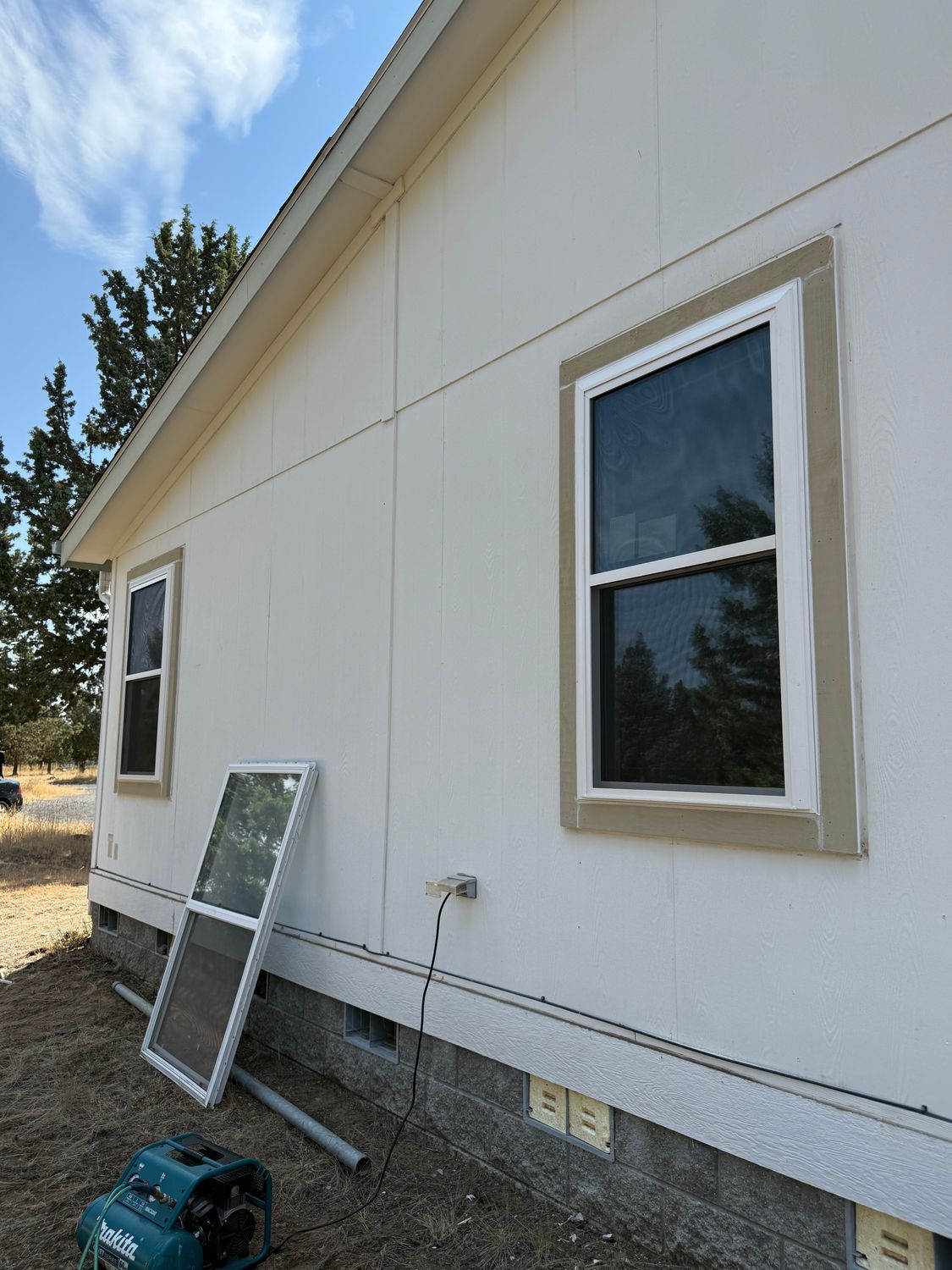 White house exterior with two windows, a screen leaning against the wall, and a blue tool on the ground