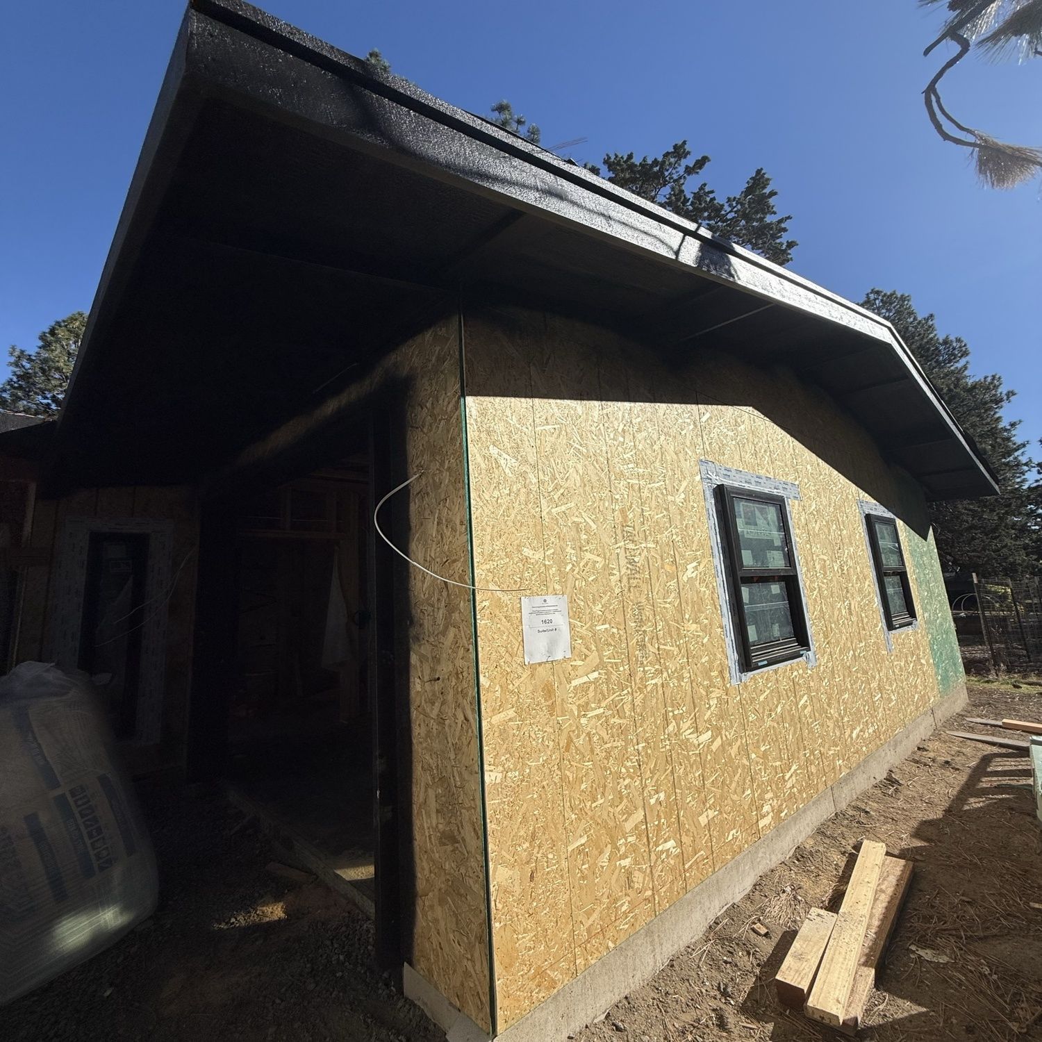 Partially built house with yellow OSB siding and a dark roof, shown from a low angle outdoors