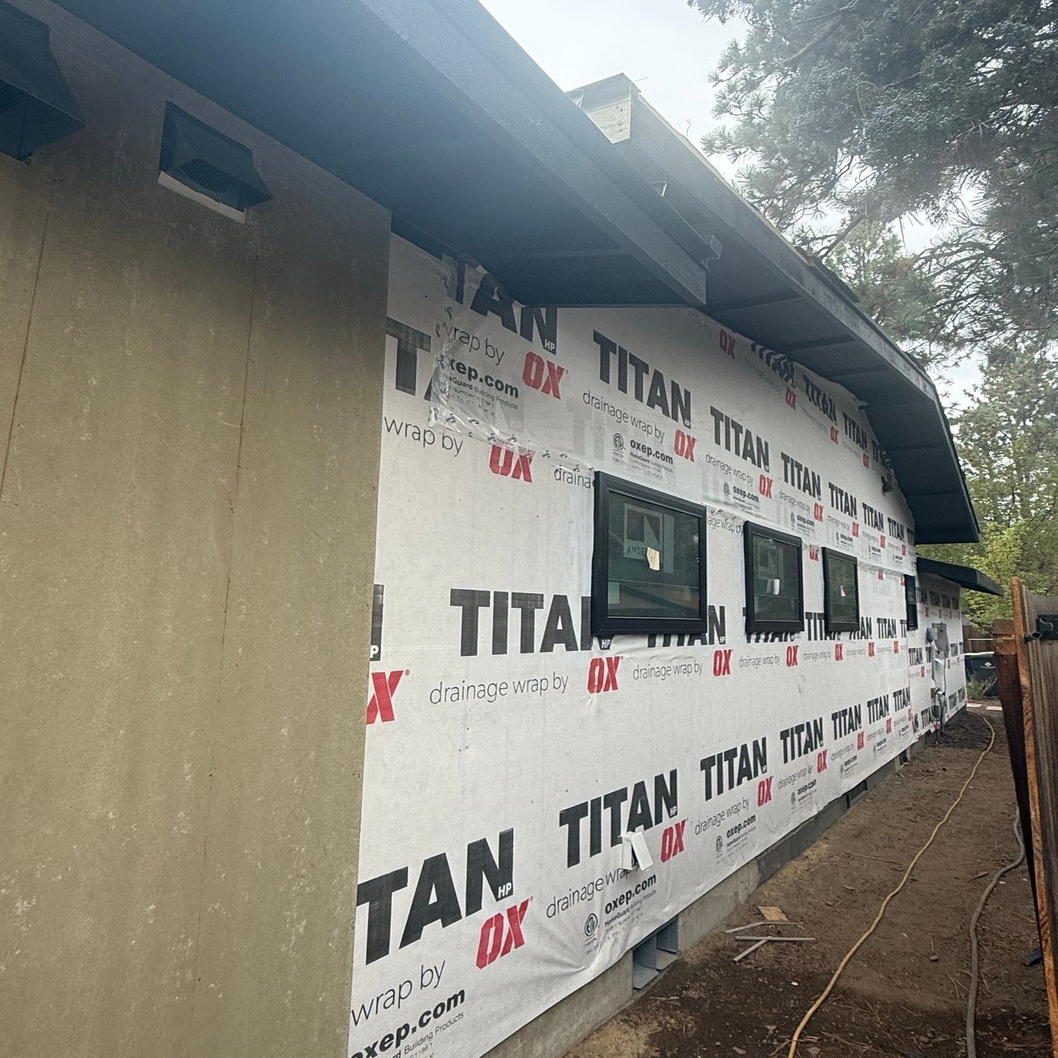 Partially wrapped house exterior with white TITAN siding, small windows, and a sloped roof.