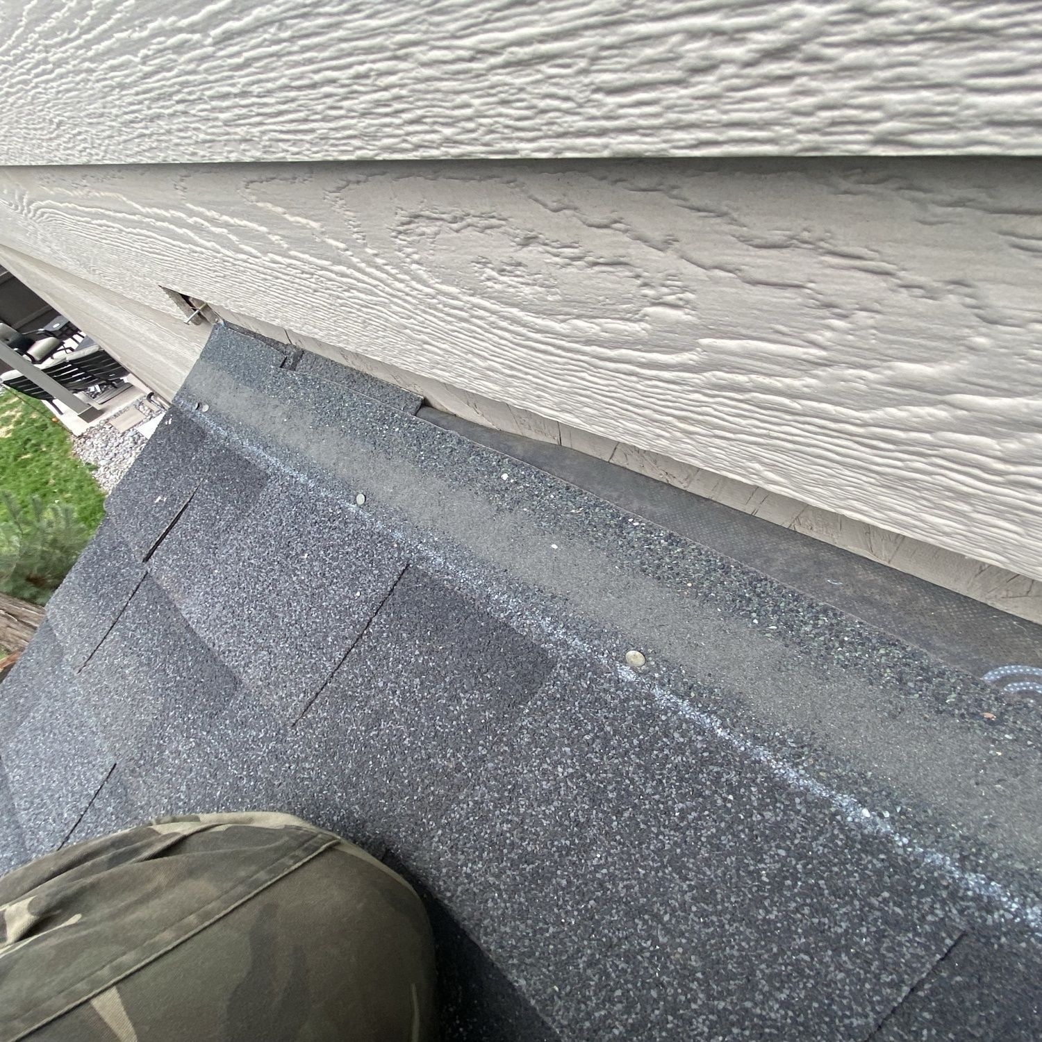 Close-up of gray roof shingles meeting beige siding along a house wall.