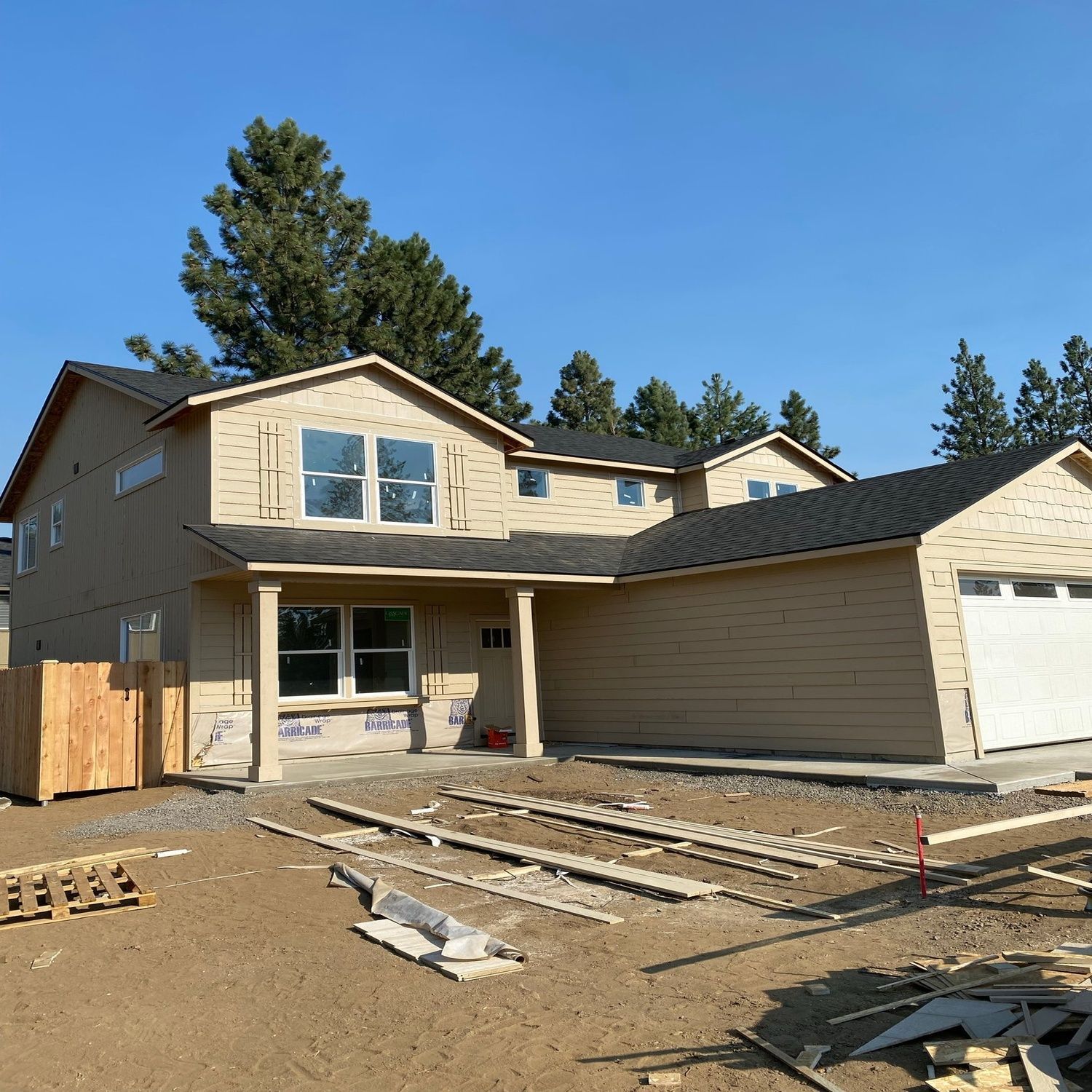 Suburban house with beige siding and garage under construction, with lumber and materials in the front yard.
