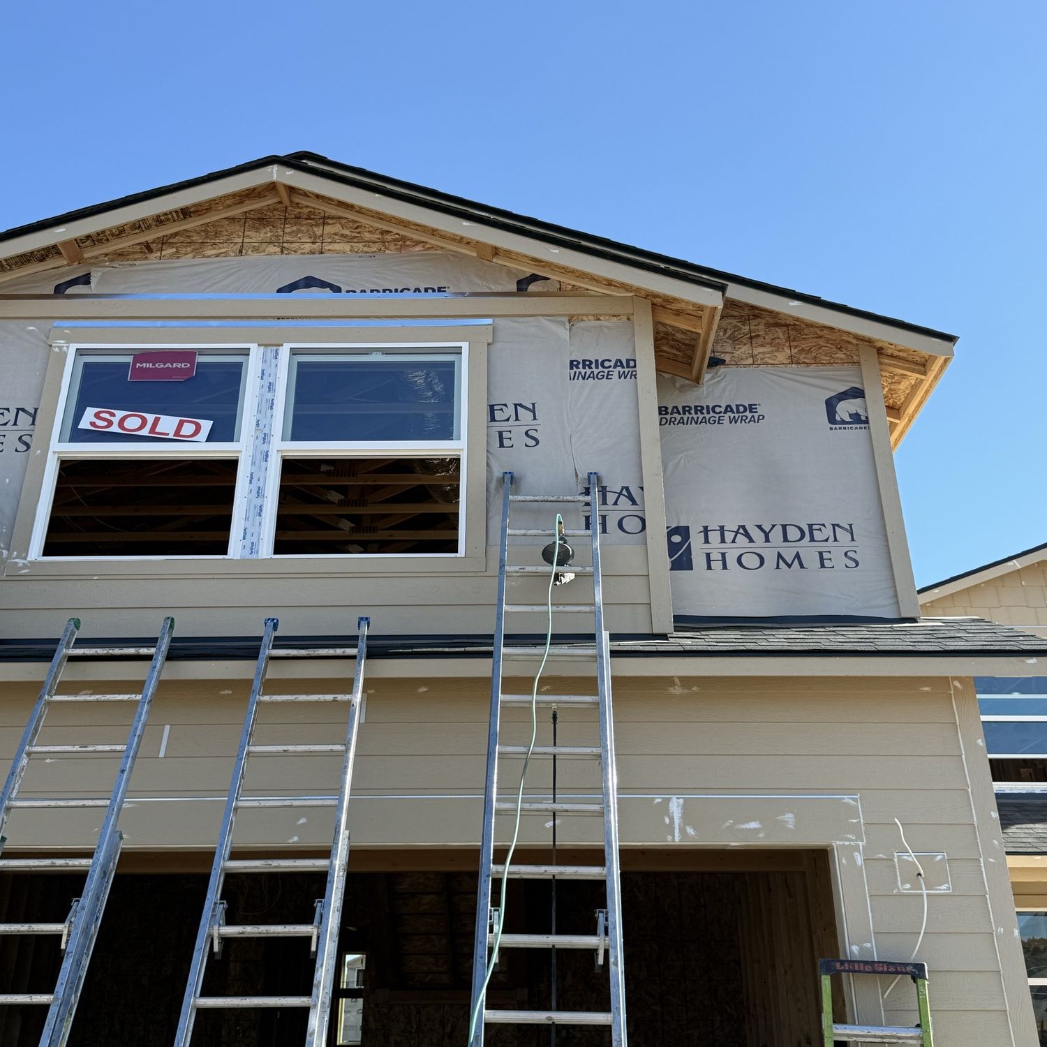 House under construction with ladders against the front and a window showing a “Sold” sign