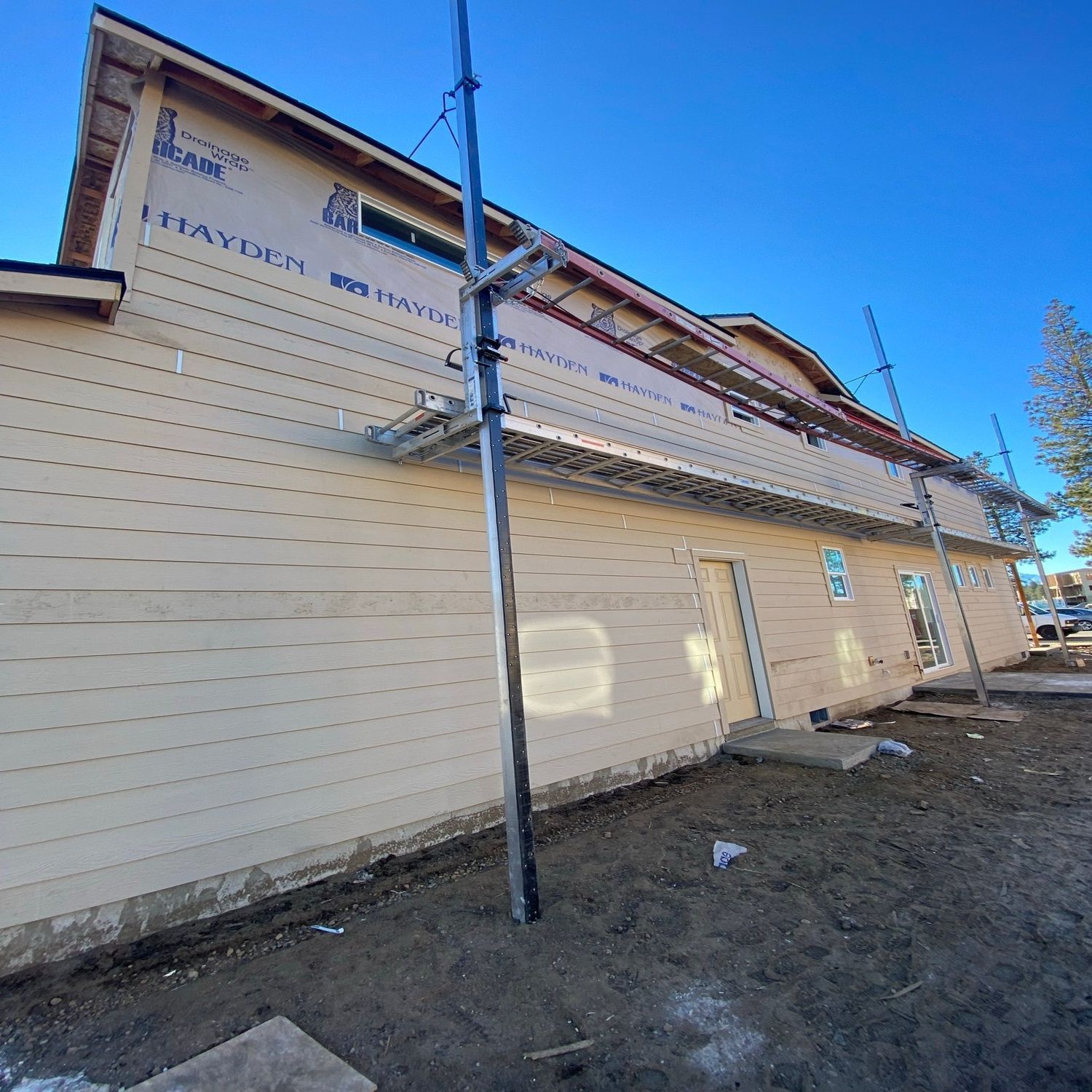 Beige two-story building exterior under a clear blue sky, with utility poles and dirt ground in front.