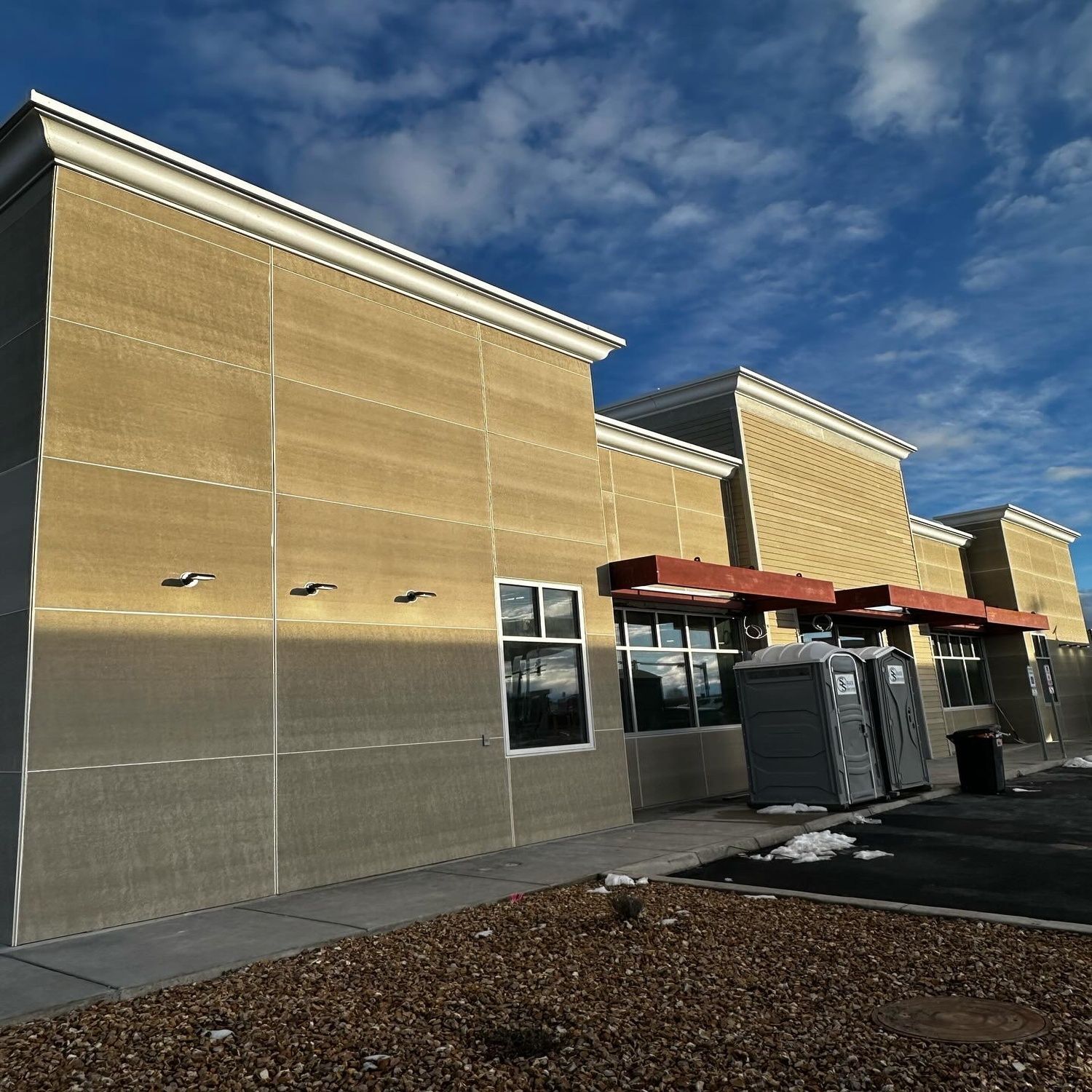 Storefront with tan brick walls, red awnings, and HVAC units under a blue sky