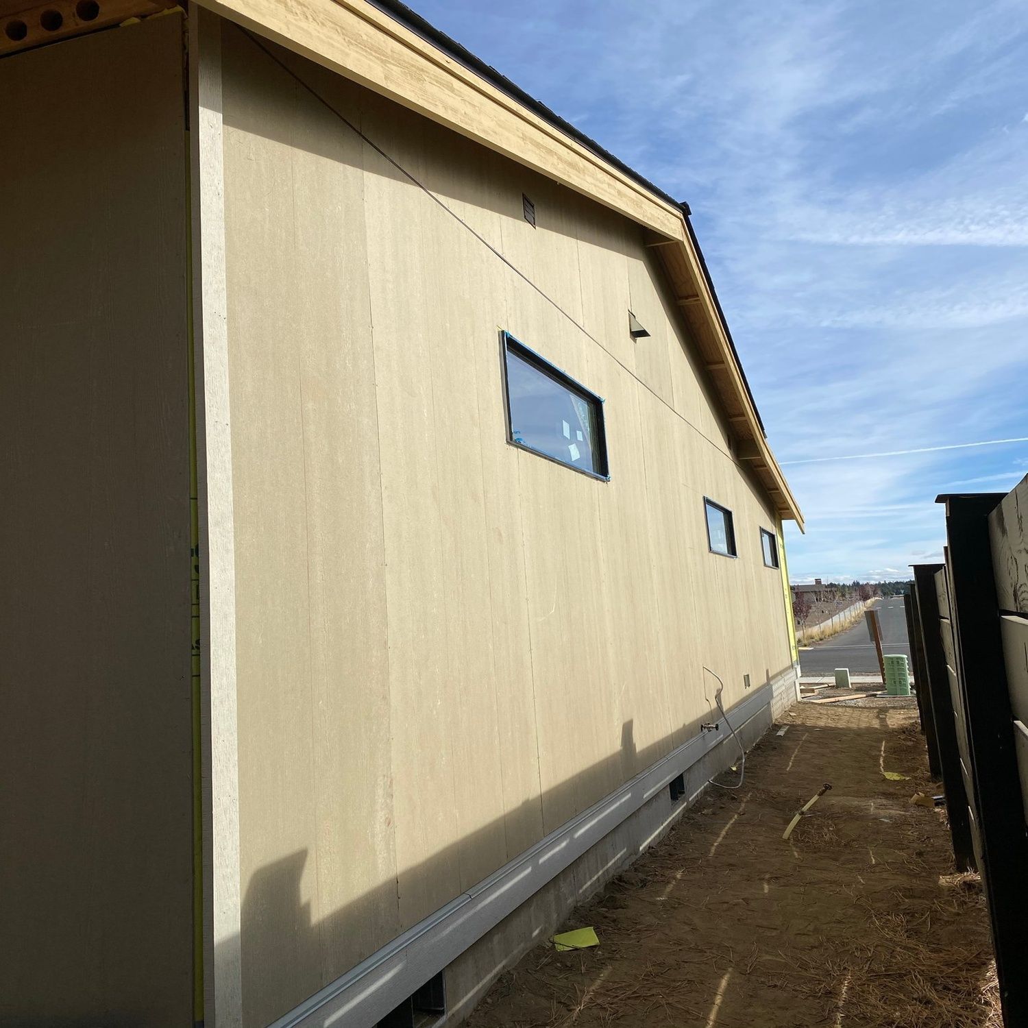 Tan exterior building wall with small windows beside a dirt path under a blue sky