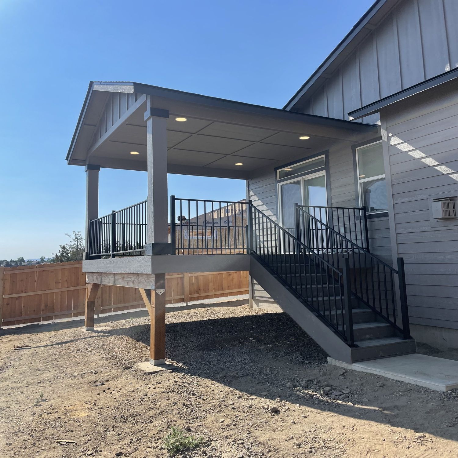 Covered back porch with steps and black railings attached to a gray house.