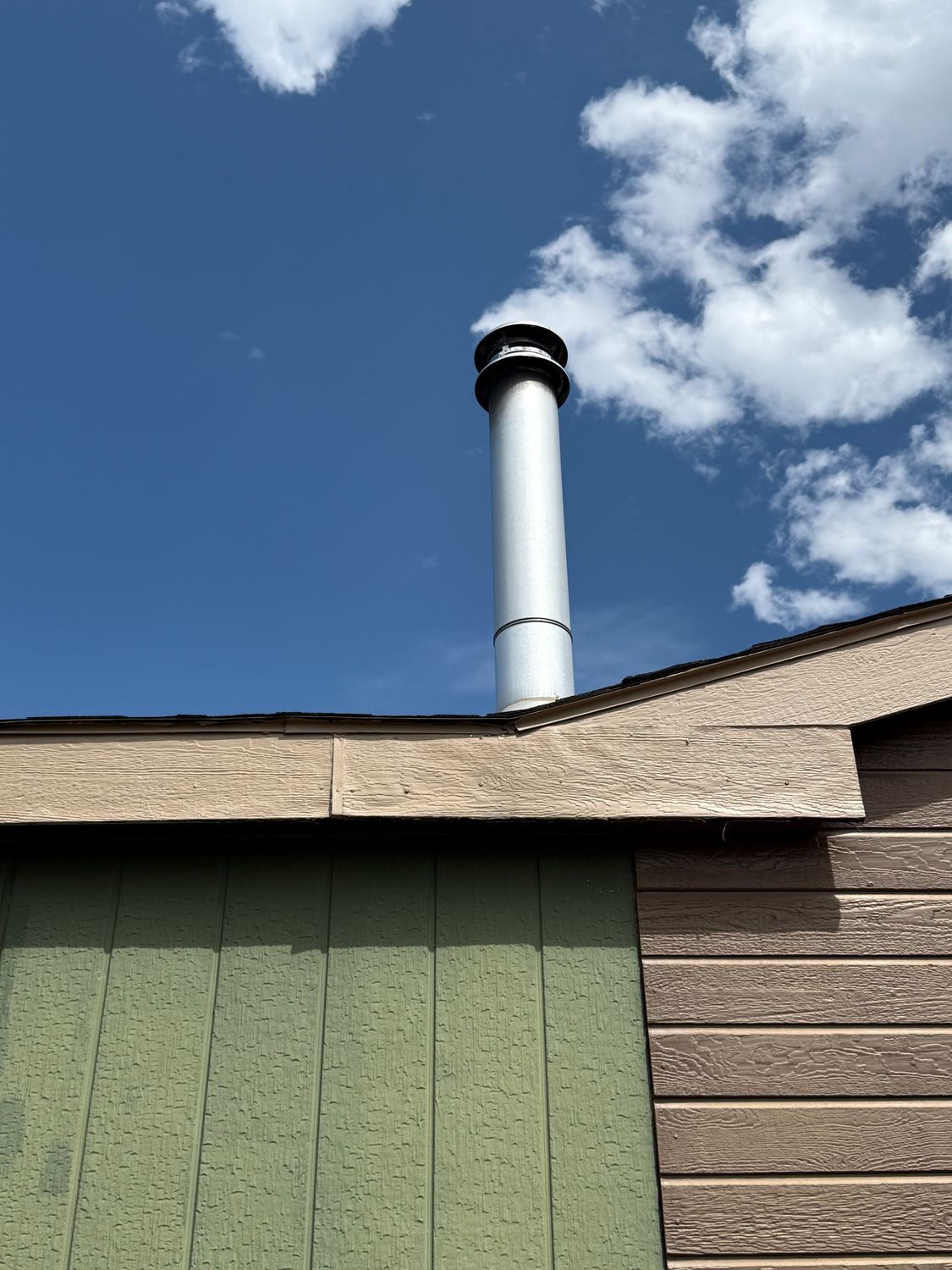 Rooftop chimney against a blue sky with scattered clouds.