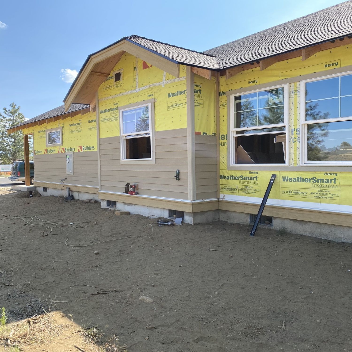 New house under construction with yellow house wrap and unfinished siding under a bright blue sky