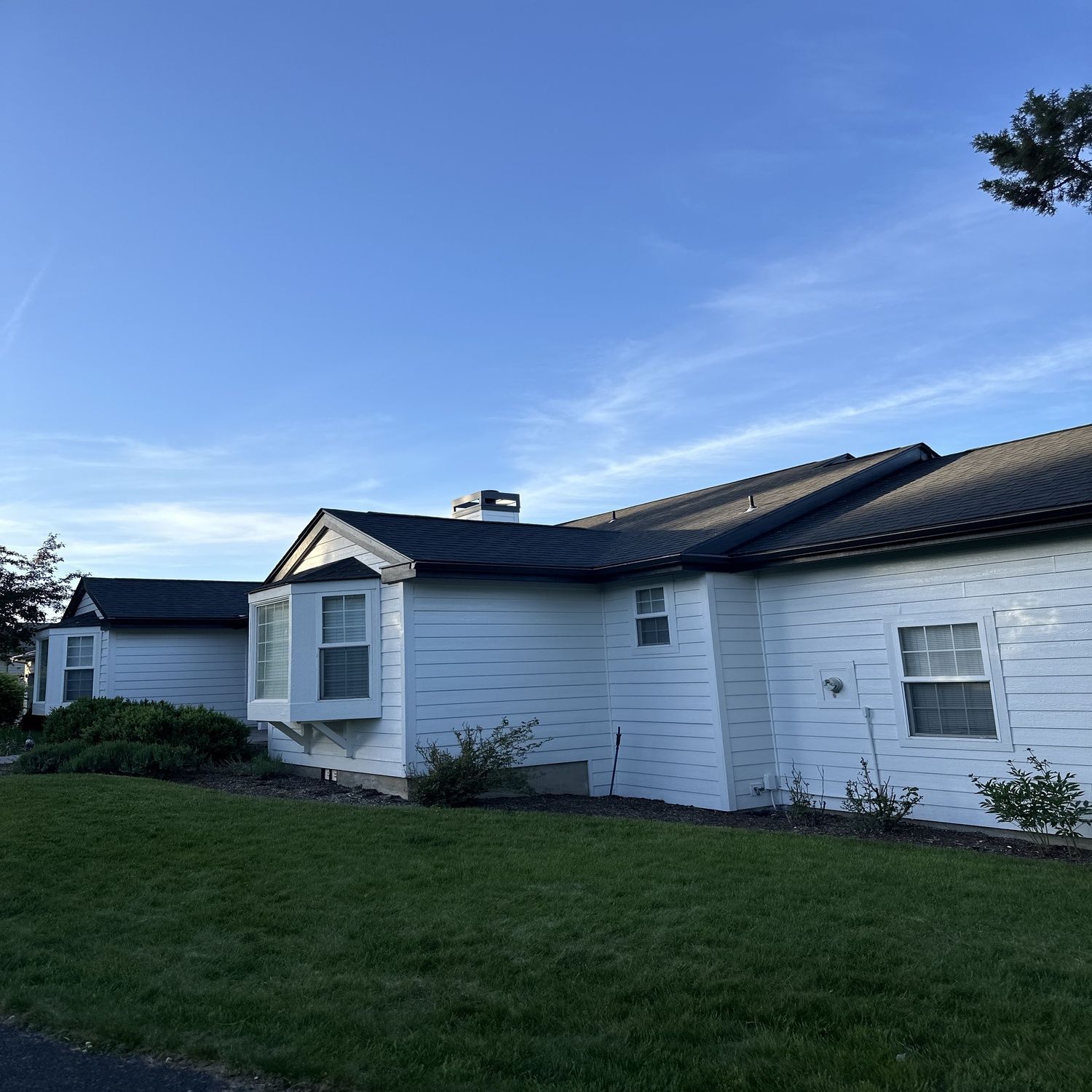White house with dark roof and green lawn under a clear blue sky.