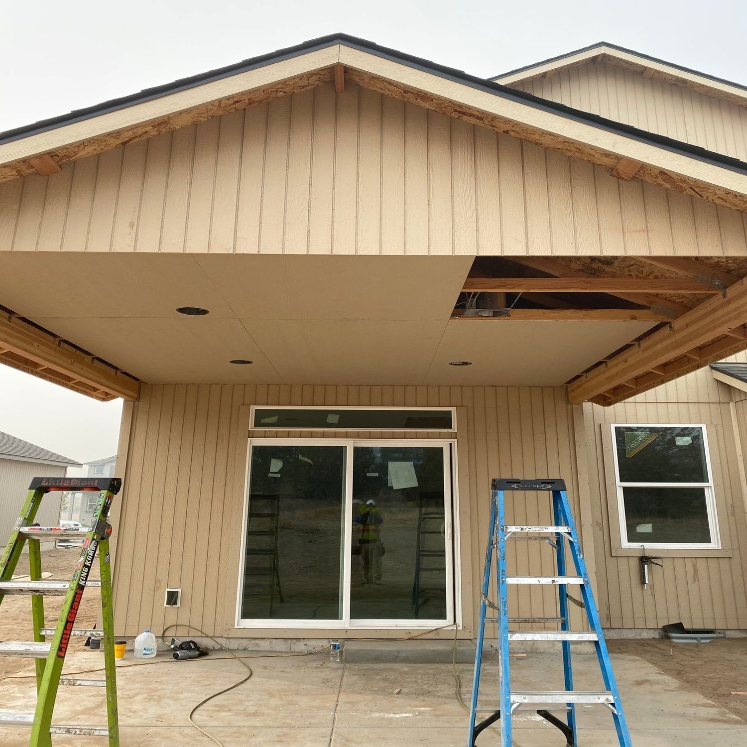 House exterior under construction with ladders and partially open siding under the porch roof