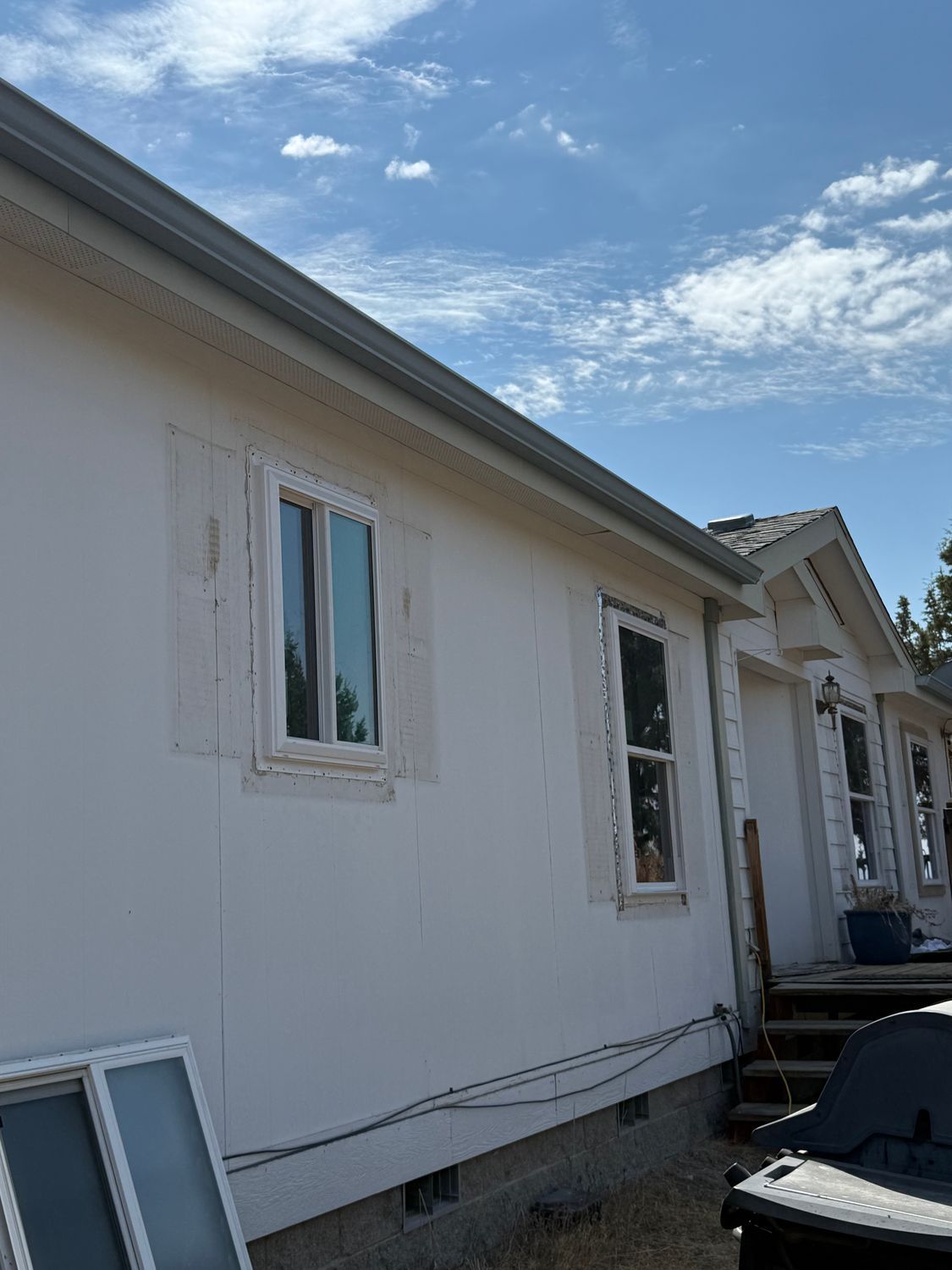 White house exterior with two windows under a blue sky, with construction materials along the side.