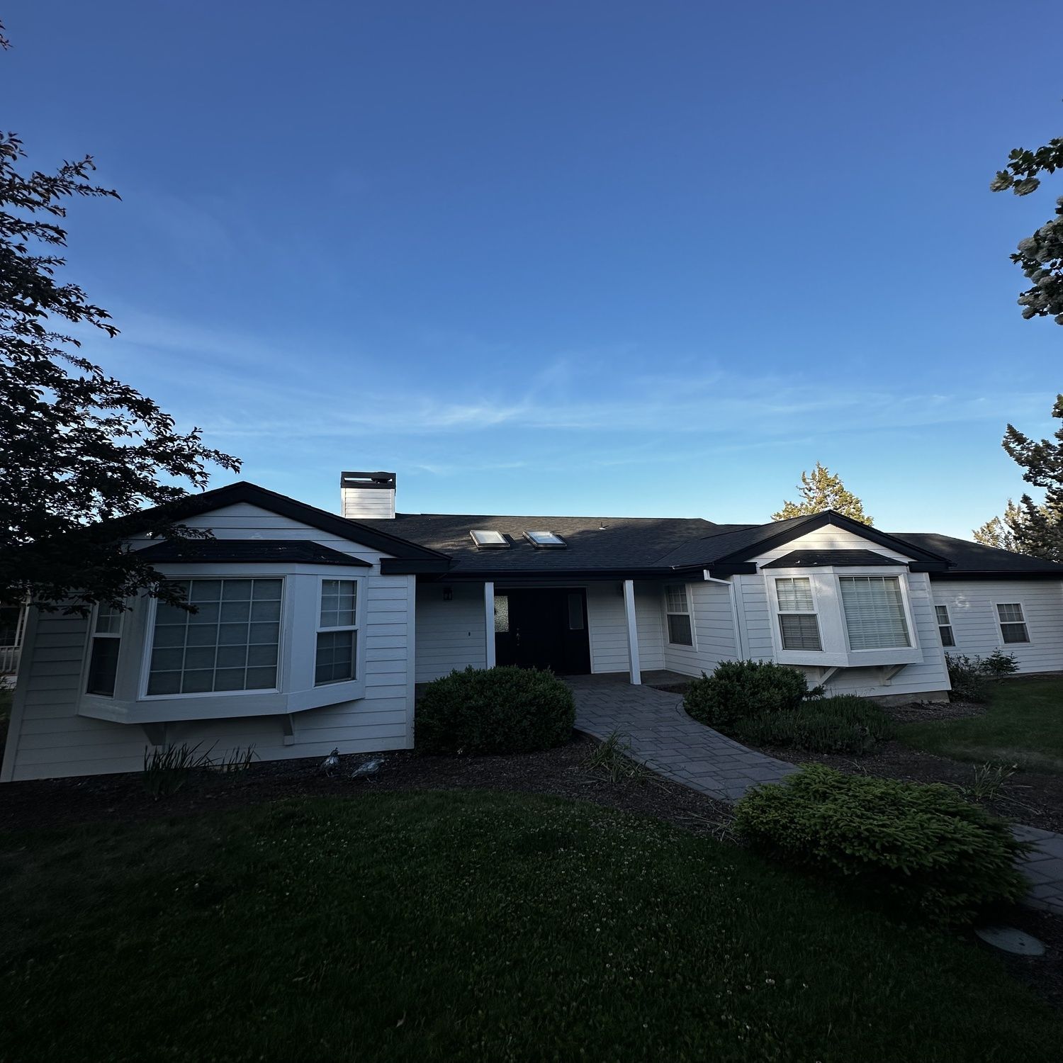Single-story white house with dark roof and central walkway under a clear blue sky